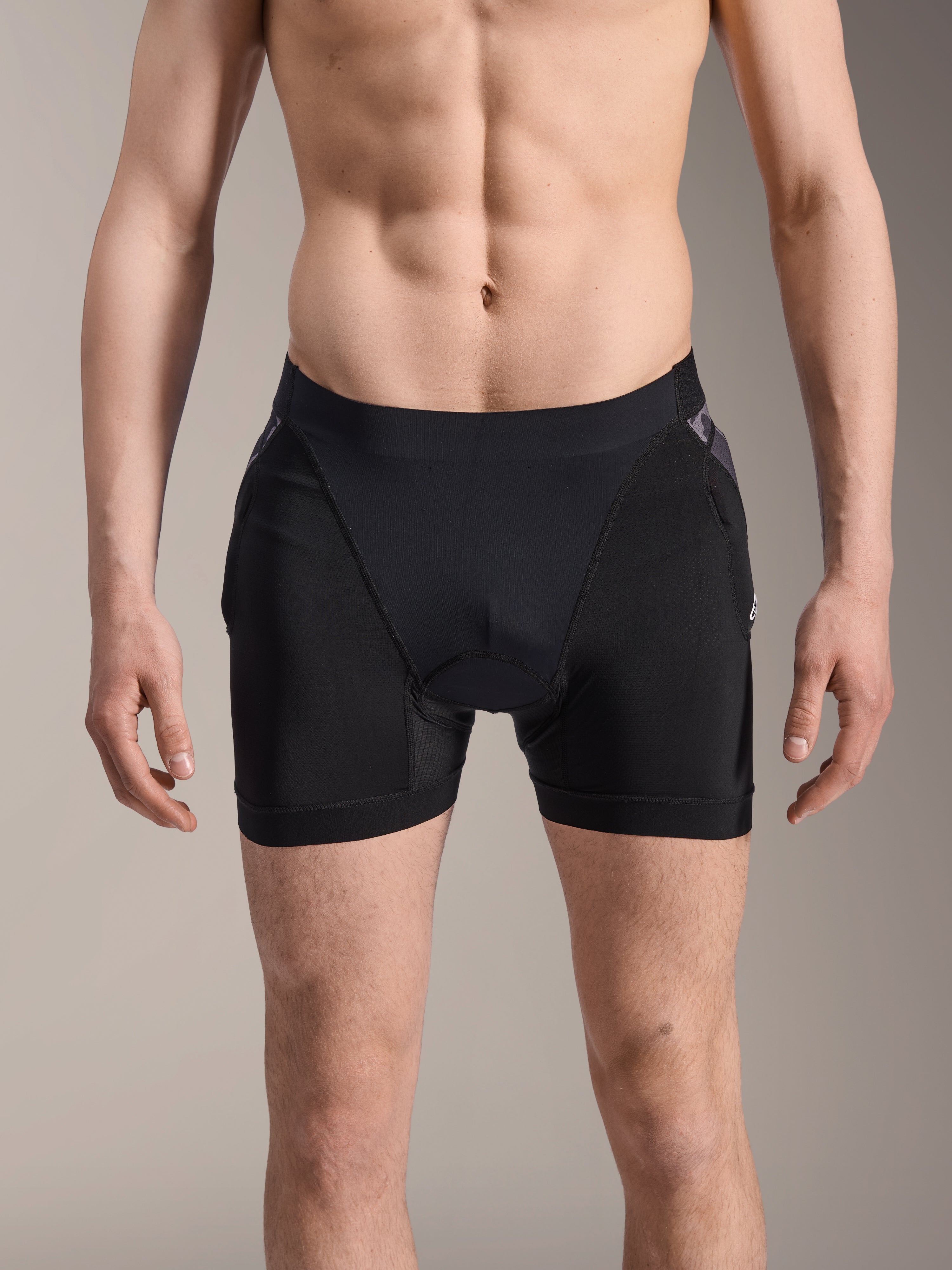 Alpinestars A-Motion Plasma Protektoren-Boxershorts, MTB-Protektorenshorts, Schwarz mit Black Camo-Akzenten, Frontansicht an männlichem Model, mit atmungsaktivem Stretch-Mesh und integriertem Hüftschutz für Radsport-Performance.