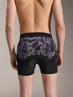 Alpinestars A-Motion Plasma Protektoren-Boxershorts, MTB-Protektorenshorts, Black Camo, Rückansicht getragen von einem Model, mit Alpinestars-Logo auf einem Camo-Mesh-Einsatz, integriertem Sitzpolster und Hüftschutztaschen, atmungsaktiver Baselayer für den Offroad-Radsport
