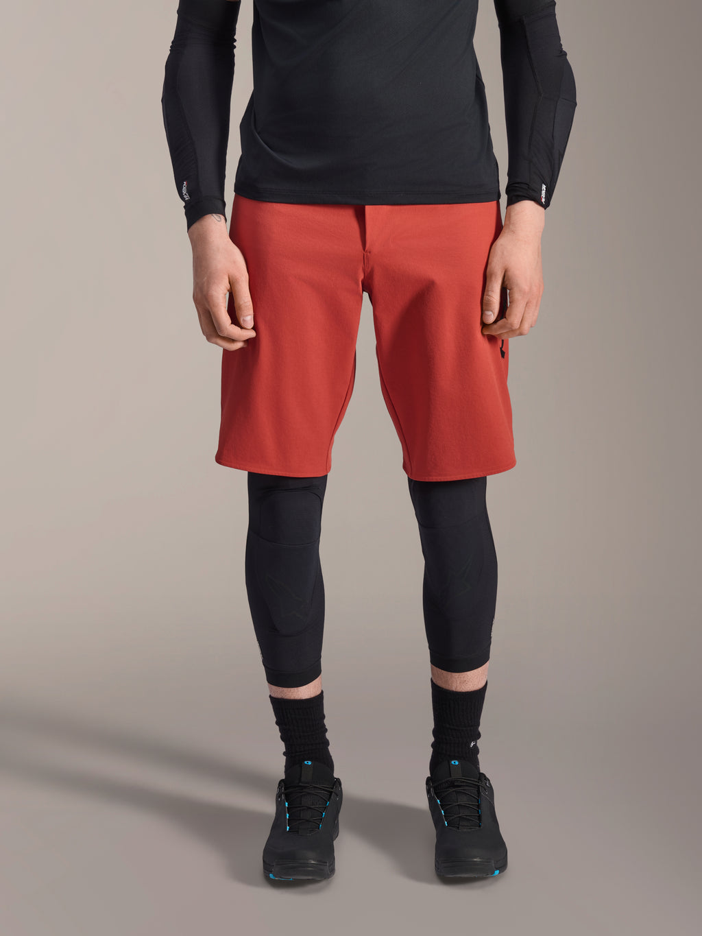 Alpinestars A-Motion Plasma Kniebandage, schwarzer MTB-Knieschützer, getragen mit roten Shorts und schwarzem Langarm-Oberteil, schlankes ergonomisches Design, leichte Mesh-Konstruktion für den Offroad-Einsatz