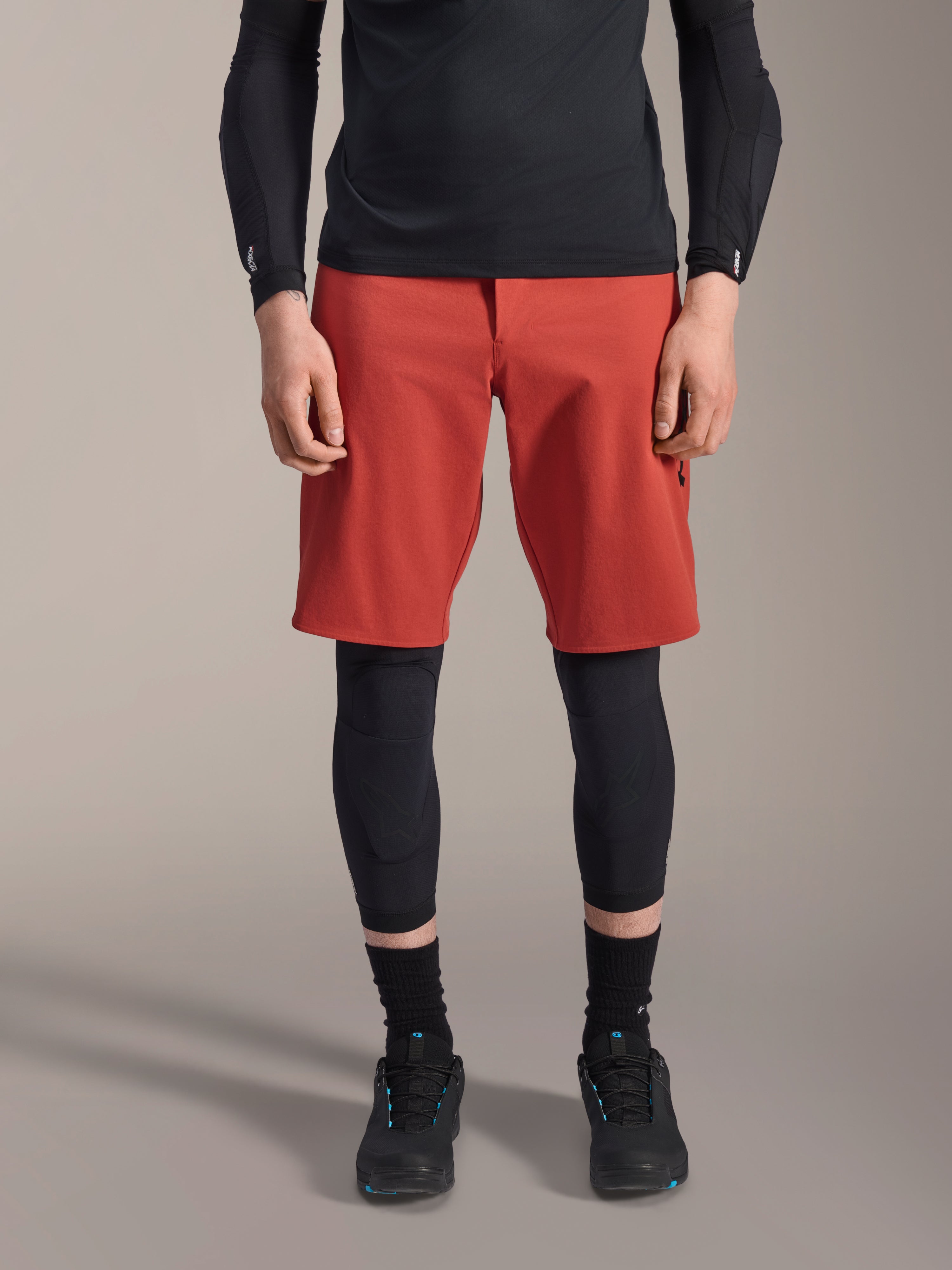 Alpinestars A-Motion Plasma Kniebandage, schwarzer MTB-Knieschützer, getragen mit roten Shorts und schwarzem Langarm-Oberteil, schlankes ergonomisches Design, leichte Mesh-Konstruktion für den Offroad-Einsatz