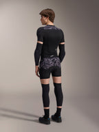 Modell trägt Alpinestars A-Motion Plasma Protektorenshorts in Black Camo und passende A-Motion Plasma Protektorenjacke, Rückansicht mit grauem Camouflage-Muster, Ellbogenprotektoren, Knieprotektoren und Radschuhe, komplette Mountainbike-Schutzausrüstung.