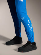 A-Supra Elite Hose in Faded Bright Blue mit weißem Astars-Logo am Unterschenkel und schwarzen MTB-Schuhen.