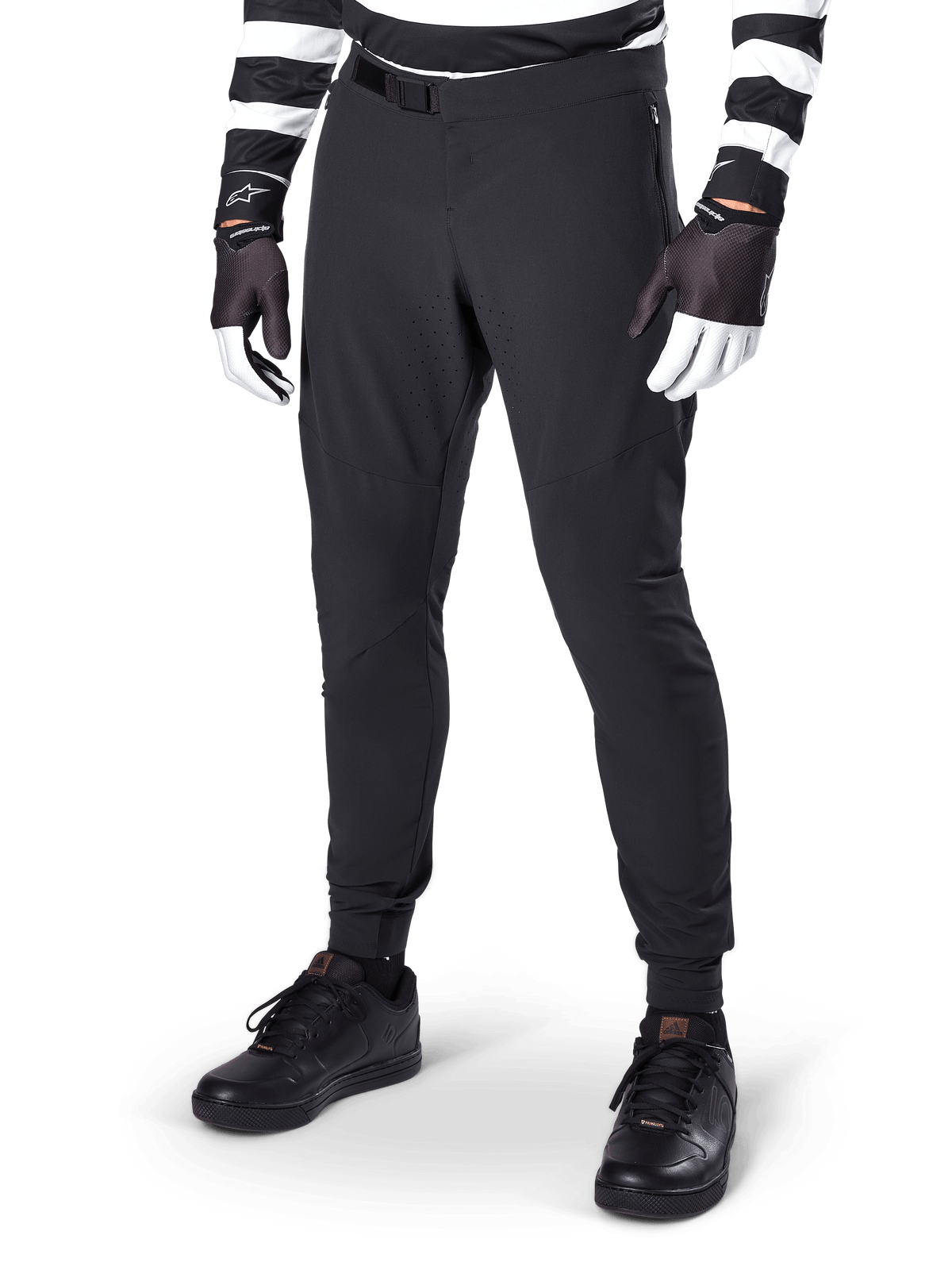 Alpinestars A-Aria Elite Hose, schwarze Mountainbike-Hose, mit lasergeschnittenen Belüftungsöffnungen an den Oberschenkeln und Magnetverschluss, getragen mit schwarz-weiß gestreiftem Trikot und Handschuhen, Performance-MTB-Ausrüstung für den Offroad-Einsatz