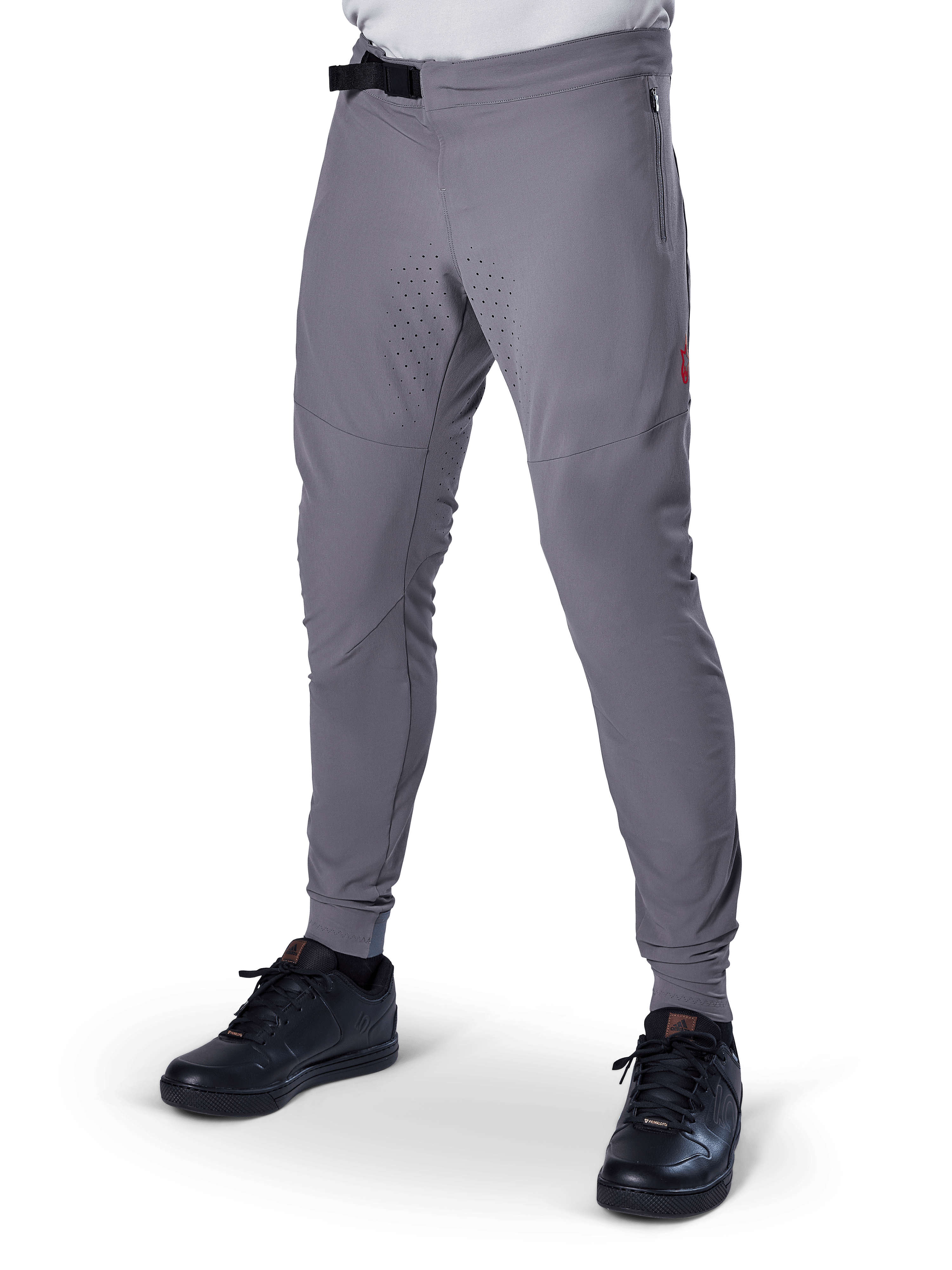Alpinestars A-Aria Elite Hose, dunkelgraue MTB-Hose, laserperforierte Einsätze an den Oberschenkeln, schwarzer Magnetverschluss, Reißverschlusstasche, rotes Logo-Detail, schmale Performance-Passform, getragen mit schwarzen Schuhen