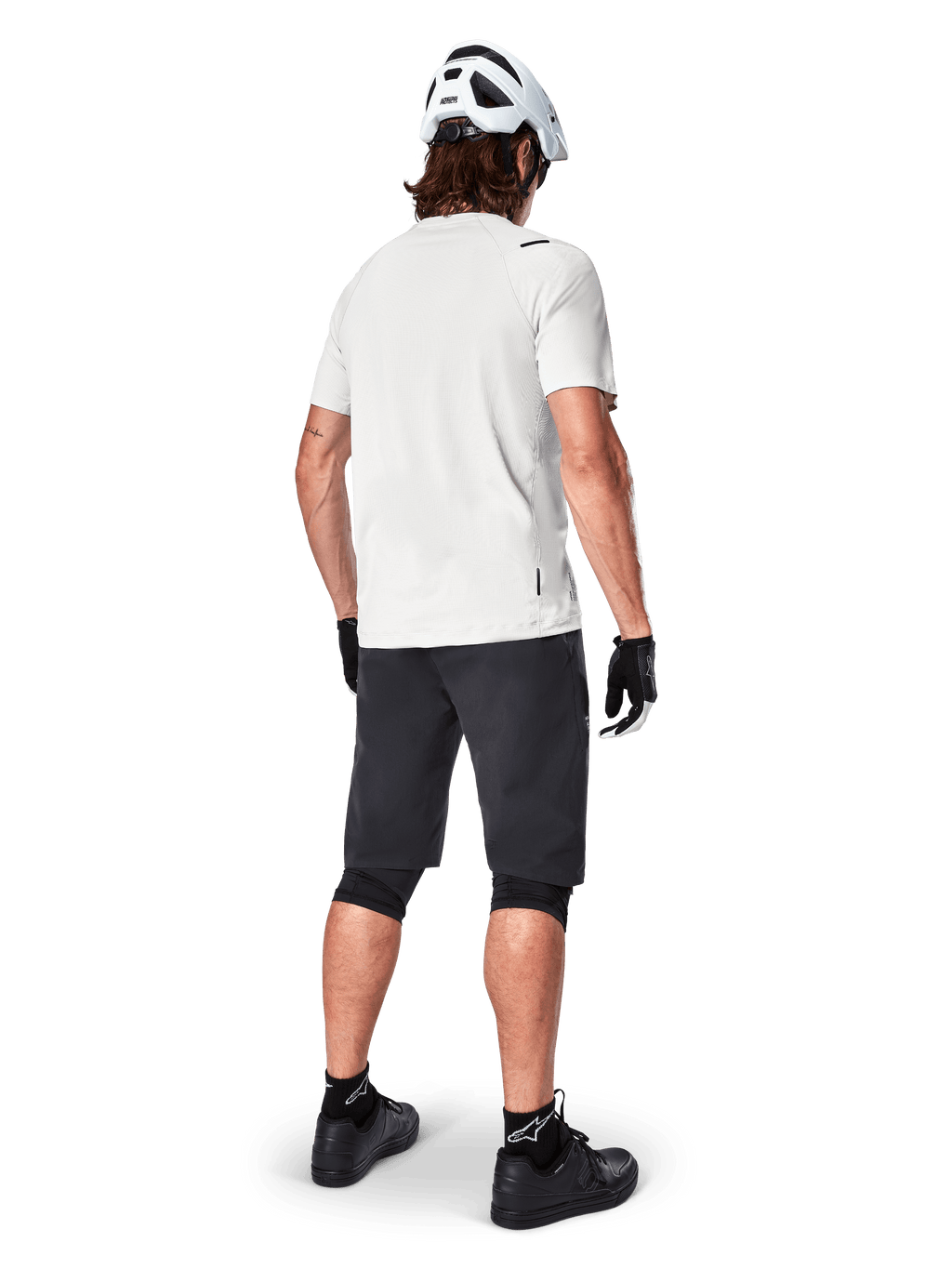 Mountain biker from behind wearing Alpinestars A-Aria Shorts in Black, white performance short-sleeve jersey, white helmet, black gloves, and black mountain bike shoes, cycling gear for trail riding