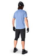 Alpinestars A-Dura Elite Shorts, Mountain Bike Shorts, Black, rear view on model, worn with light blue short-sleeve shirt and black protective gear, technical design with zippered pockets and reflective details for off-road cycling