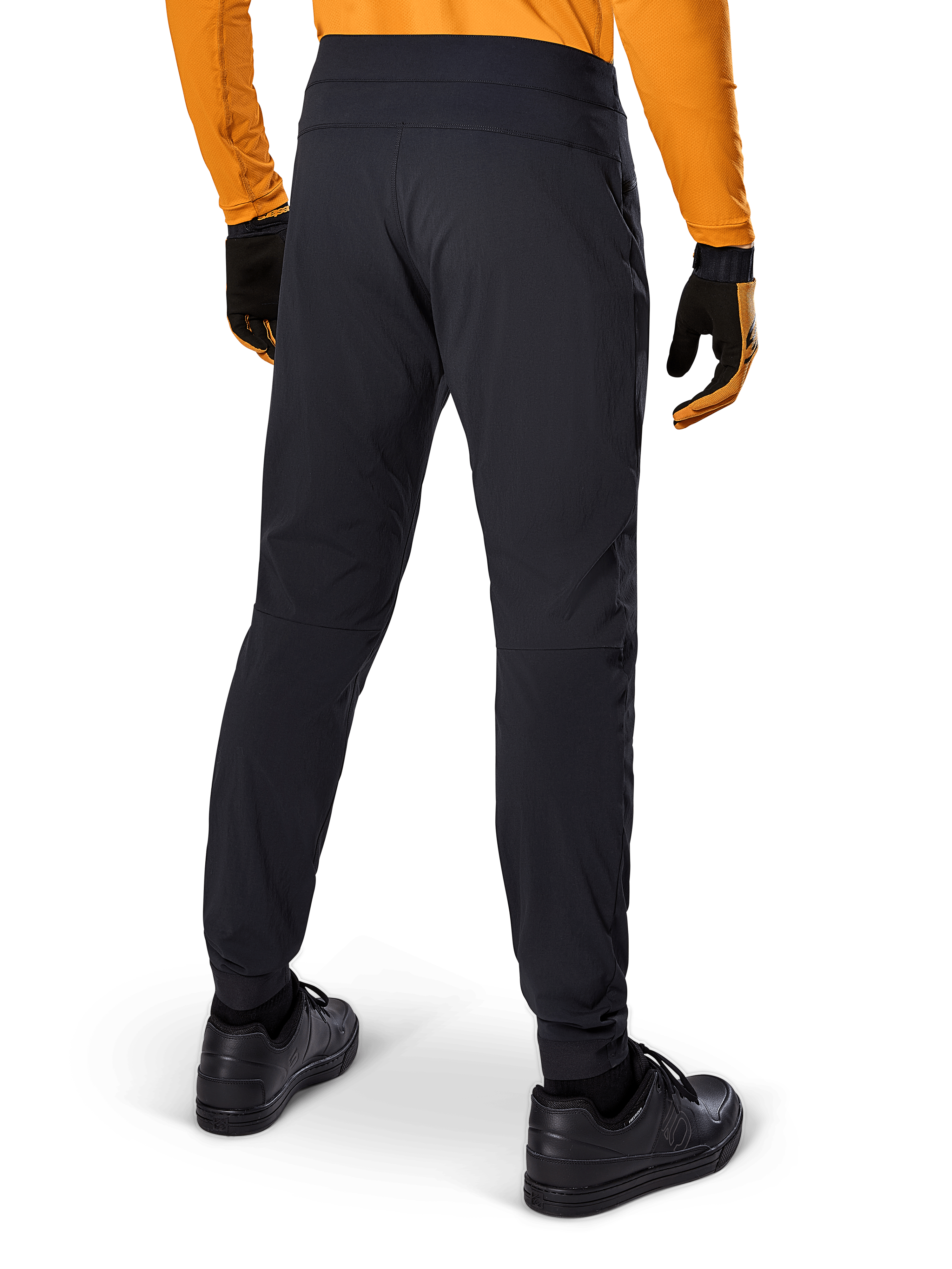 Alpinestars A-Dura Pants, Black MTB Pants, rear view, worn with an orange long-sleeve jersey and black gloves, featuring elasticated cuffs and durable textile material for mountain biking.
