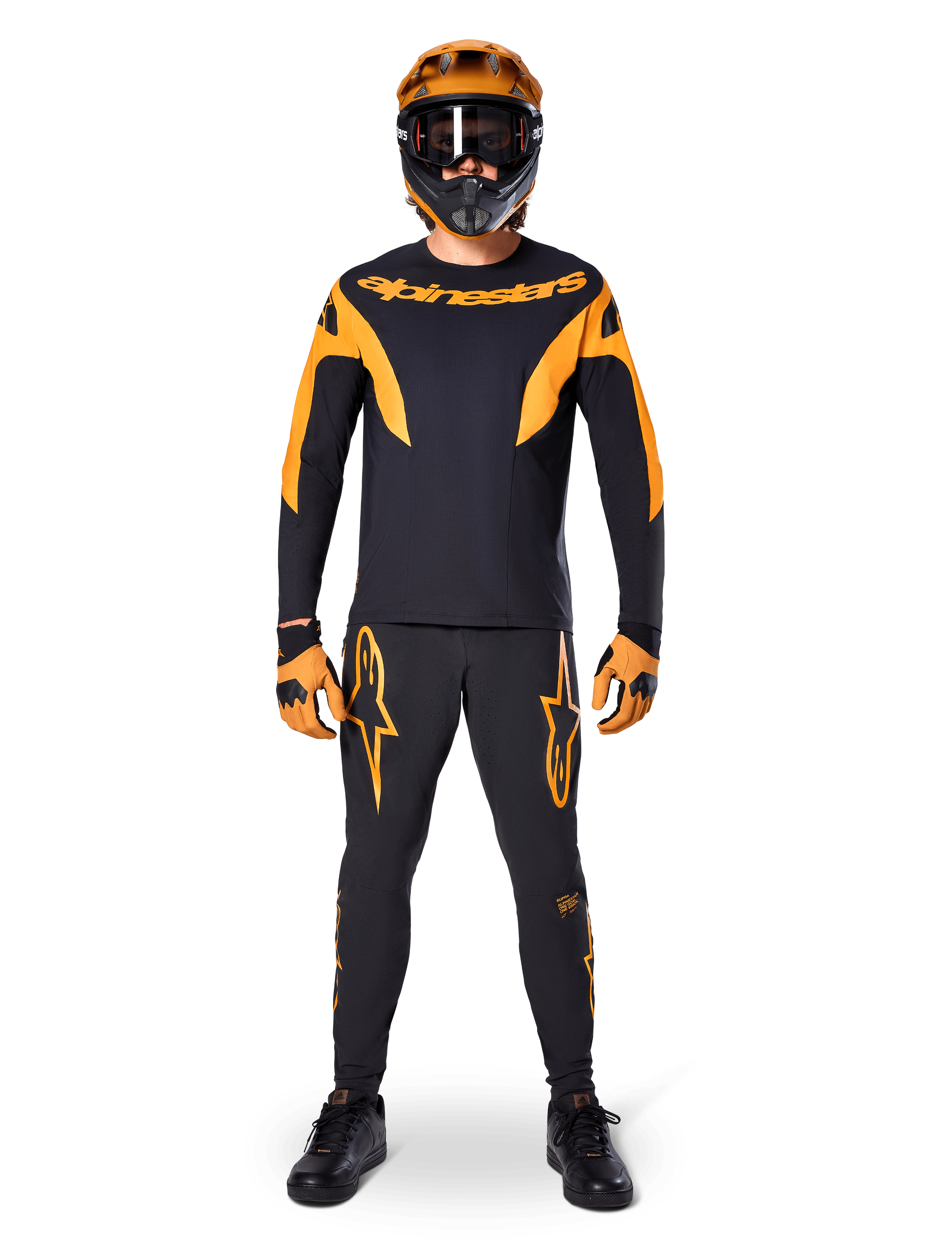 Alpinestars A-Supra Race Pants, MTB Racing Pants, Black and Orange, worn by a rider in a complete racing kit including a black and orange jersey, orange helmet, and matching gloves, featuring bold orange star logos on the legs