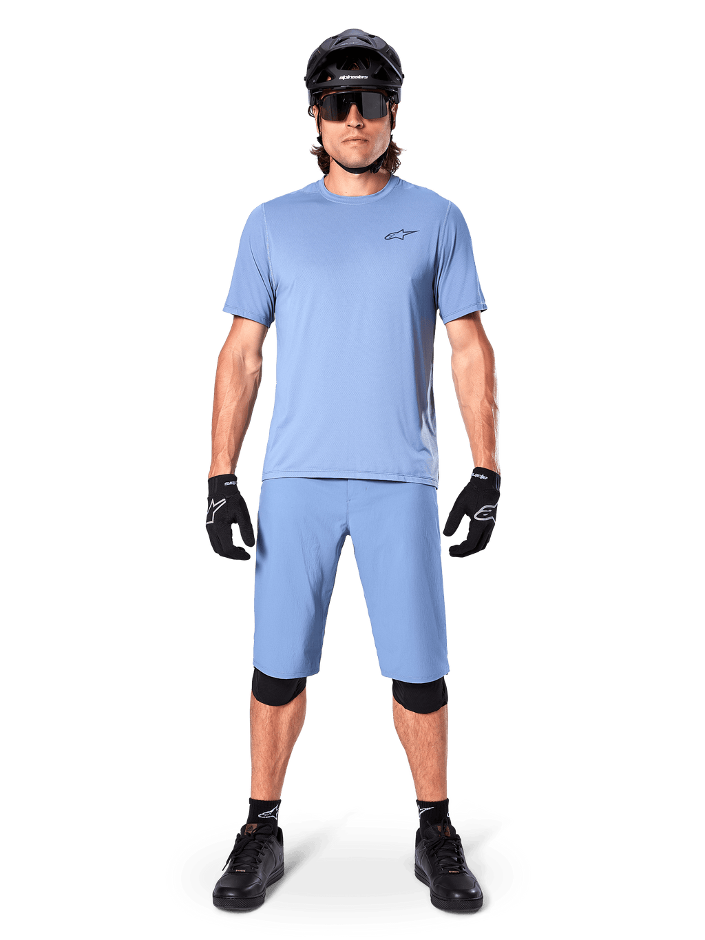 Model trägt Alpinestars A-Dura Shorts in Infinity Blue, passendes hellblaues Trikot, schwarzen Mountainbike-Helm, schwarze Sonnenbrille, schwarze Handschuhe und Knieschoner, komplettes MTB-Outfit für Trailfahrten