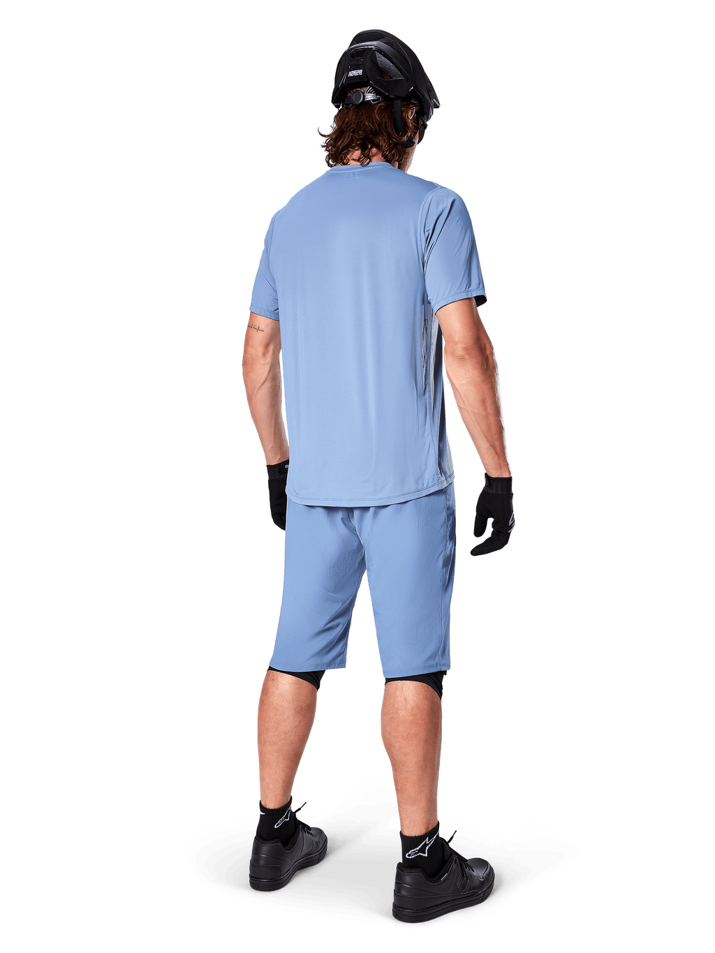 Rückansicht eines Mountainbikers in Alpinestars A-Dura Shorts in Infinity Blue, passendes Kurzarmtrikot, schwarzer Helm, schwarze Handschuhe und schwarze Schuhe, abgestimmte Performance-Ausrüstung für MTB-Trailfahrten