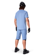 Rückansicht eines Mountainbikers in Alpinestars A-Dura Shorts in Infinity Blue, passendes Kurzarmtrikot, schwarzer Helm, schwarze Handschuhe und schwarze Schuhe, abgestimmte Performance-Ausrüstung für MTB-Trailfahrten