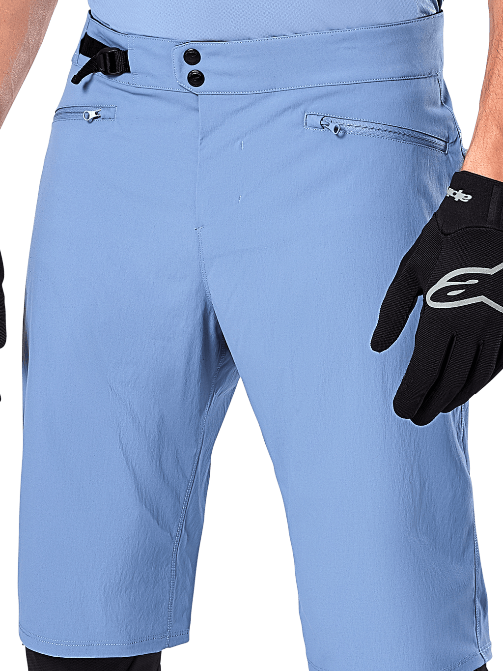 Alpinestars A-Dura Shorts, Mountainbike-Shorts in Infinity Blue, Nahaufnahme der Taille mit doppeltem Druckknopfverschluss, verstellbarem seitlichem Taillenversteller und Reißverschlusstaschen mit Mesh-Futter, getragen mit einem schwarzen Alpinestars-Handschuh