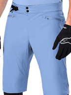 Alpinestars A-Dura Shorts, Mountainbike-Shorts in Infinity Blue, Nahaufnahme der Taille mit doppeltem Druckknopfverschluss, verstellbarem seitlichem Taillenversteller und Reißverschlusstaschen mit Mesh-Futter, getragen mit einem schwarzen Alpinestars-Handschuh