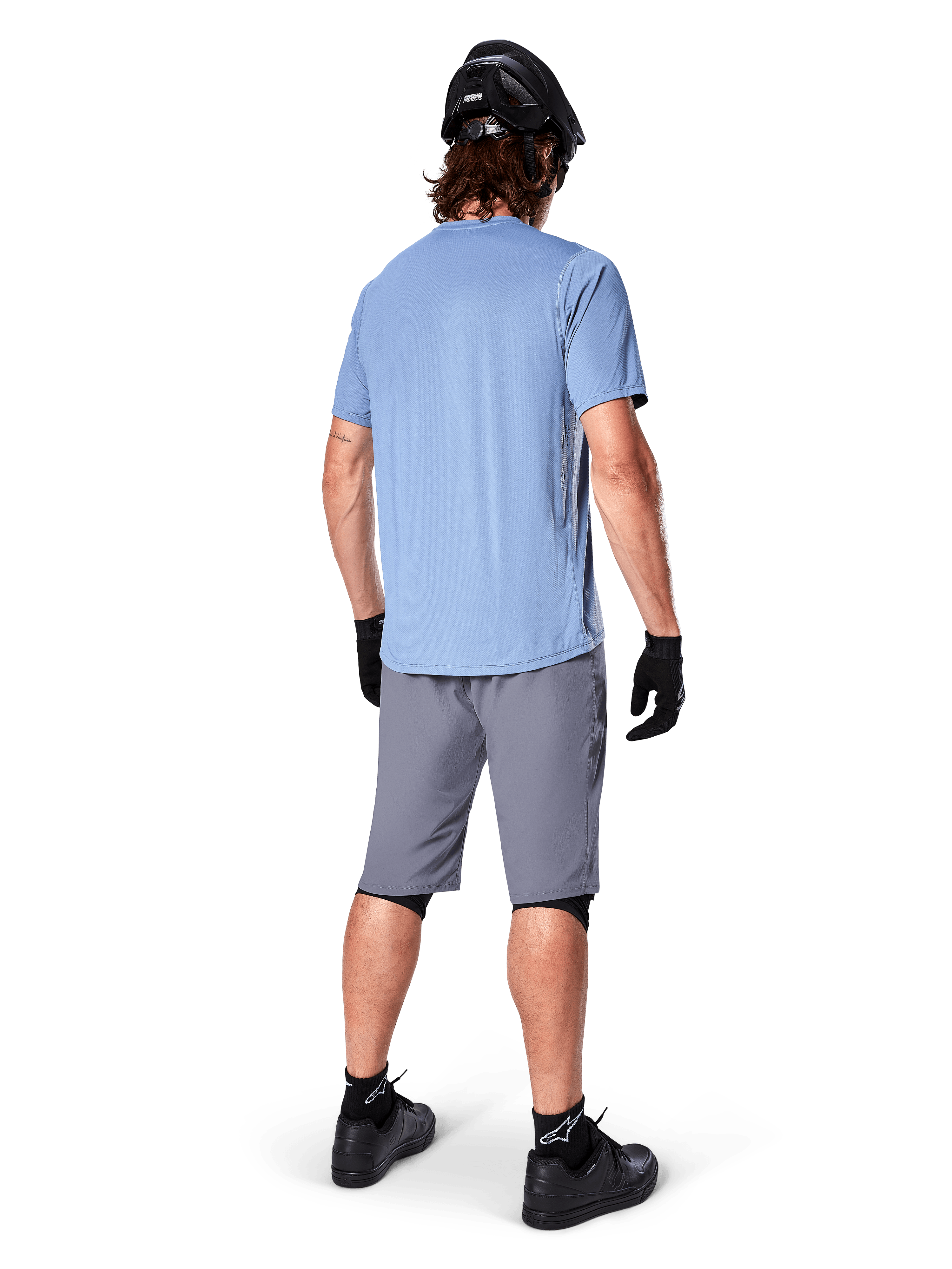 Alpinestars A-Dura Shorts, Dark Gray MTB Shorts, rear view, worn with a light blue short-sleeve jersey and black mountain bike helmet, black gloves and socks with black shoes, functional and durable gear for off-road cycling