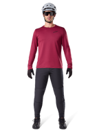 Männliches Model im Alpinestars A-Dura Thermal Jersey in Burgundy, langärmeliges isoliertes Radsport-Oberteil, kombiniert mit dunkelgrauer Mountainbike-Hose, weißem Helm, schwarzer Sonnenbrille und schwarzen Handschuhen, professionelle MTB-Ausrüstung für kaltes Wetter