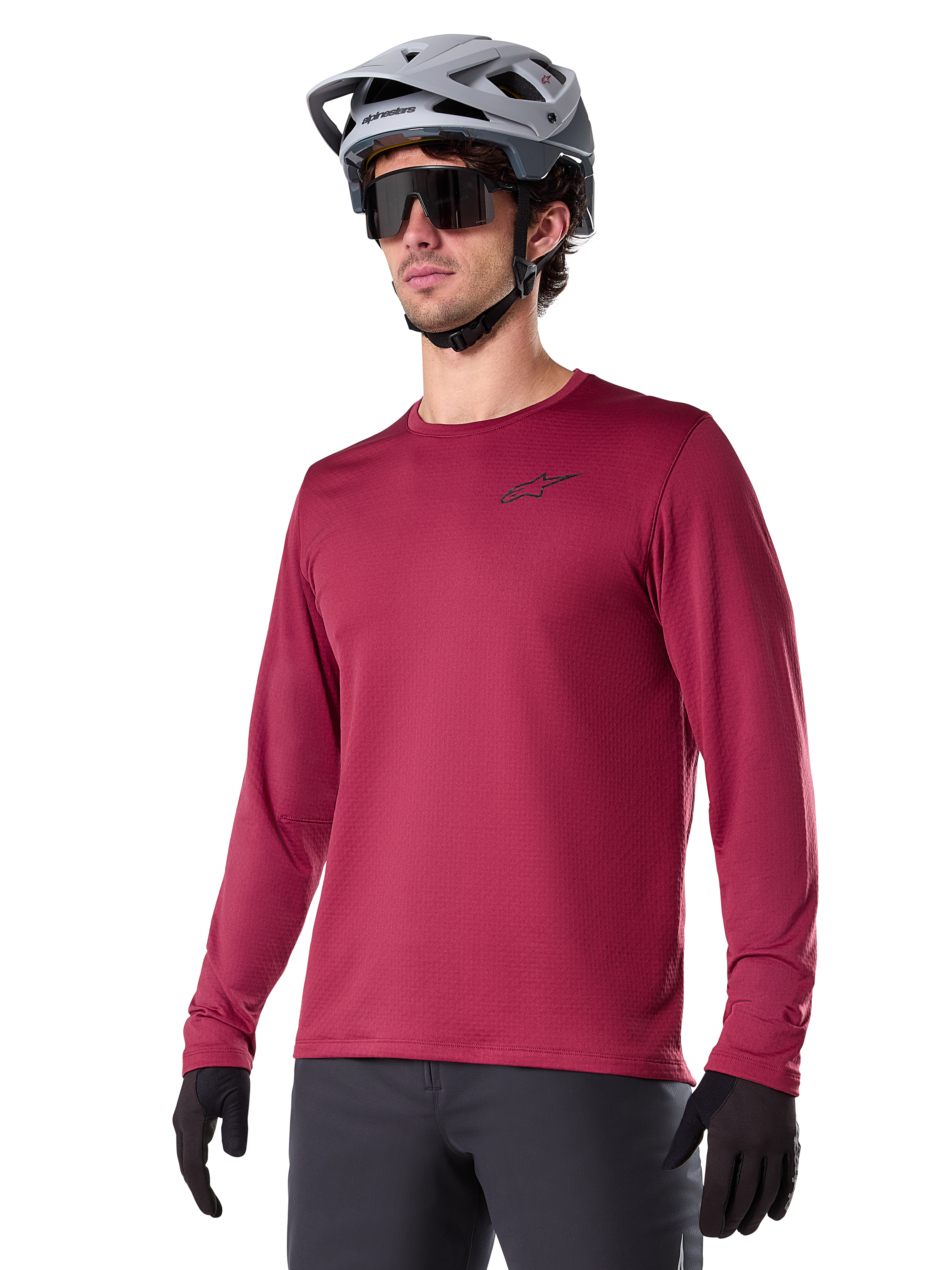Alpinestars A-Dura Thermal Jersey, Langarm-Mountainbike-Trikot, Burgunderrot, mit isoliertem Fleece-Futter und kleinem schwarzem Brust-Logo, getragen mit einem grauen Helm, schwarzer Sonnenbrille und schwarzen Handschuhen, ideal für Radsport bei kaltem Wetter