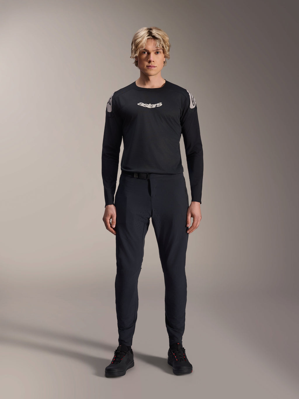 Alpinestars A-Aria Polartec Elite Langarm-Trikot in Schwarz, männliches Model mit weißem Astars-Logo auf der Brust und Branding an den Schultern, kombiniert mit schwarzer technischer MTB-Hose und Schuhen, Performance-Mountainbike-Ausrüstung