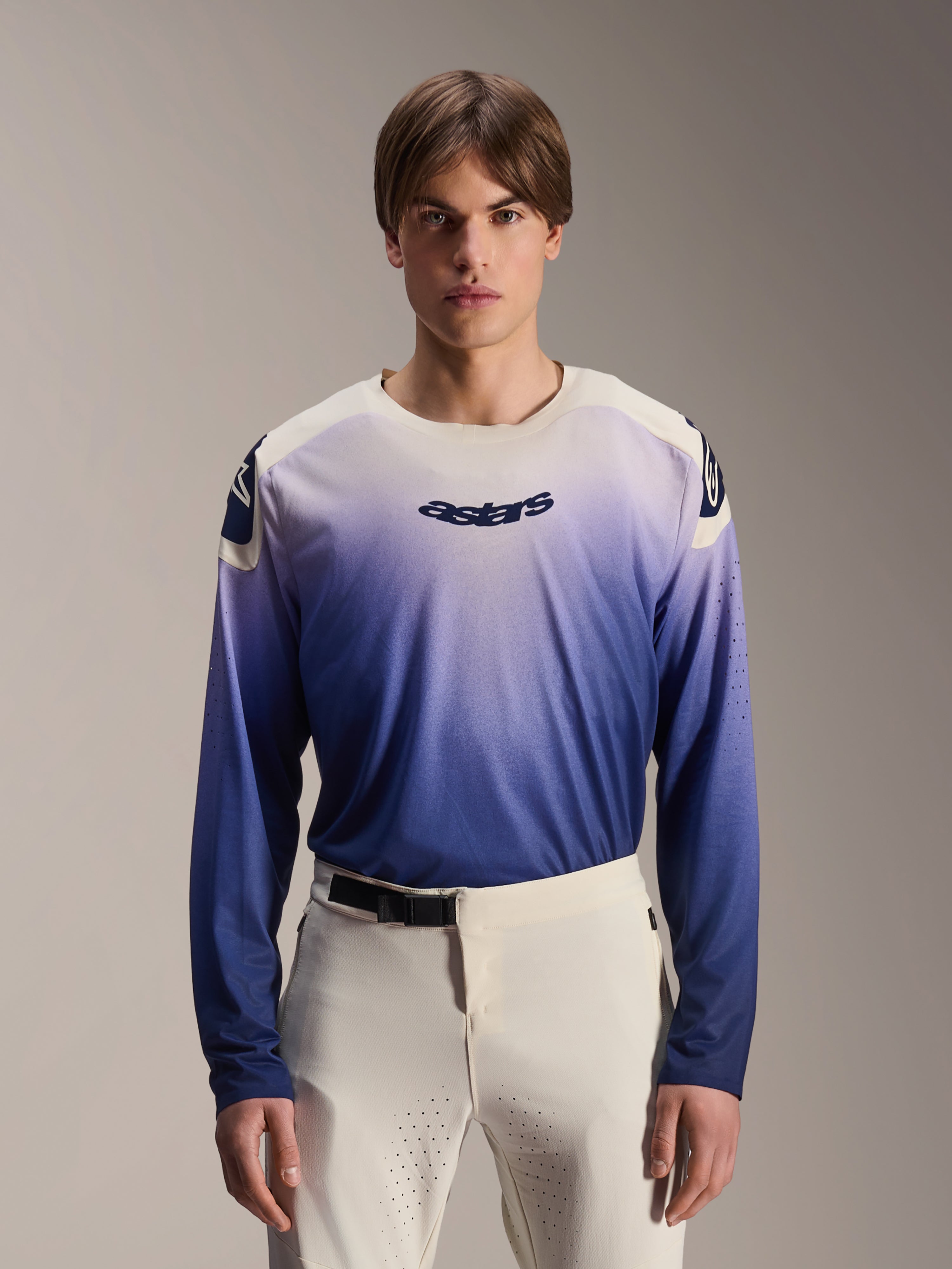Alpinestars A-Aria Polartec Maker Elite Trikot, Langarm-MTB-Trikot, Baja Blue mit weiß-blauem Farbverlauf, von einem Model mit weißer Hose getragen, mit dunkelblauem Logo auf der Brust und Laserperforationen an den Ärmeln, Performance-Mountainbike-Bekleidung