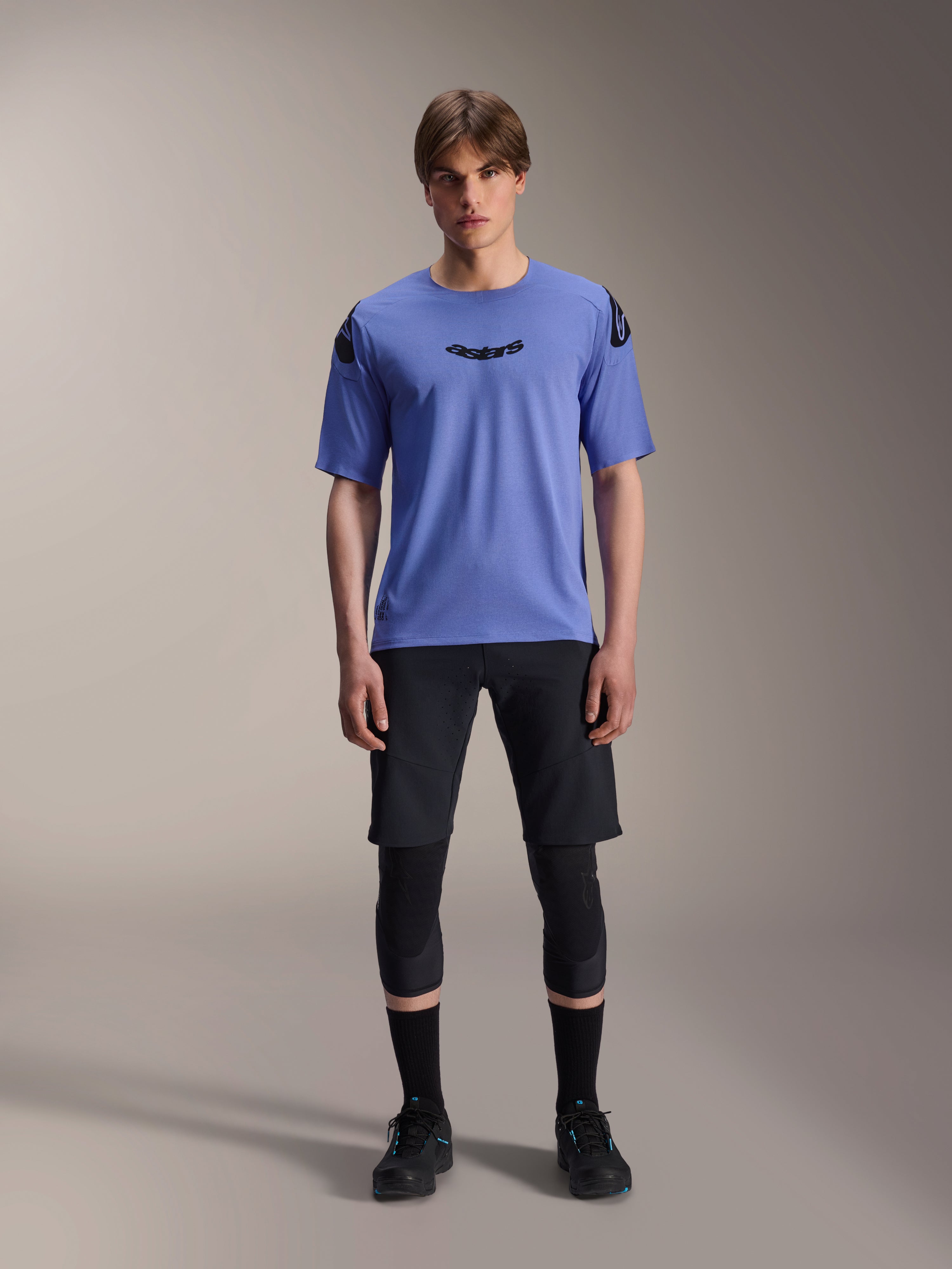 Alpinestars A-Aria Lite Short, Herren-Mountainbike-Shorts, Schwarz, getragen mit hellviolettem Kurzarm-Trikot und schwarzen Knieschonern, Performance-MTB-Bekleidung