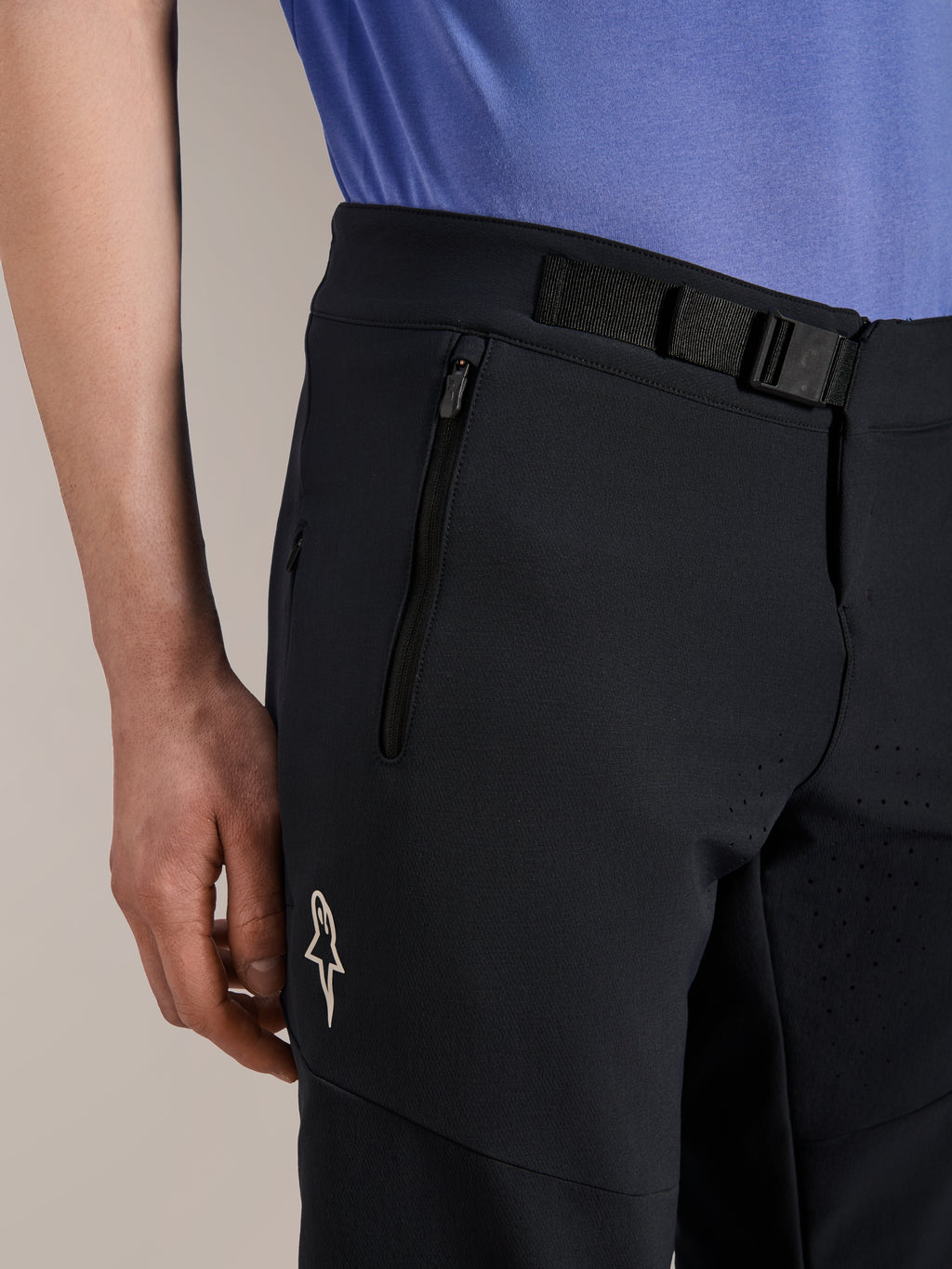 Alpinestars A-Aria Elite Shorts, Mountainbike-Shorts, Black Titanium, mit magnetischem Schnallenverschluss, Reißverschlusstasche und weißem Alpinestars-Logo, getragen mit einem blauen Radtrikot, Performance-Mountainbike-Ausrüstung