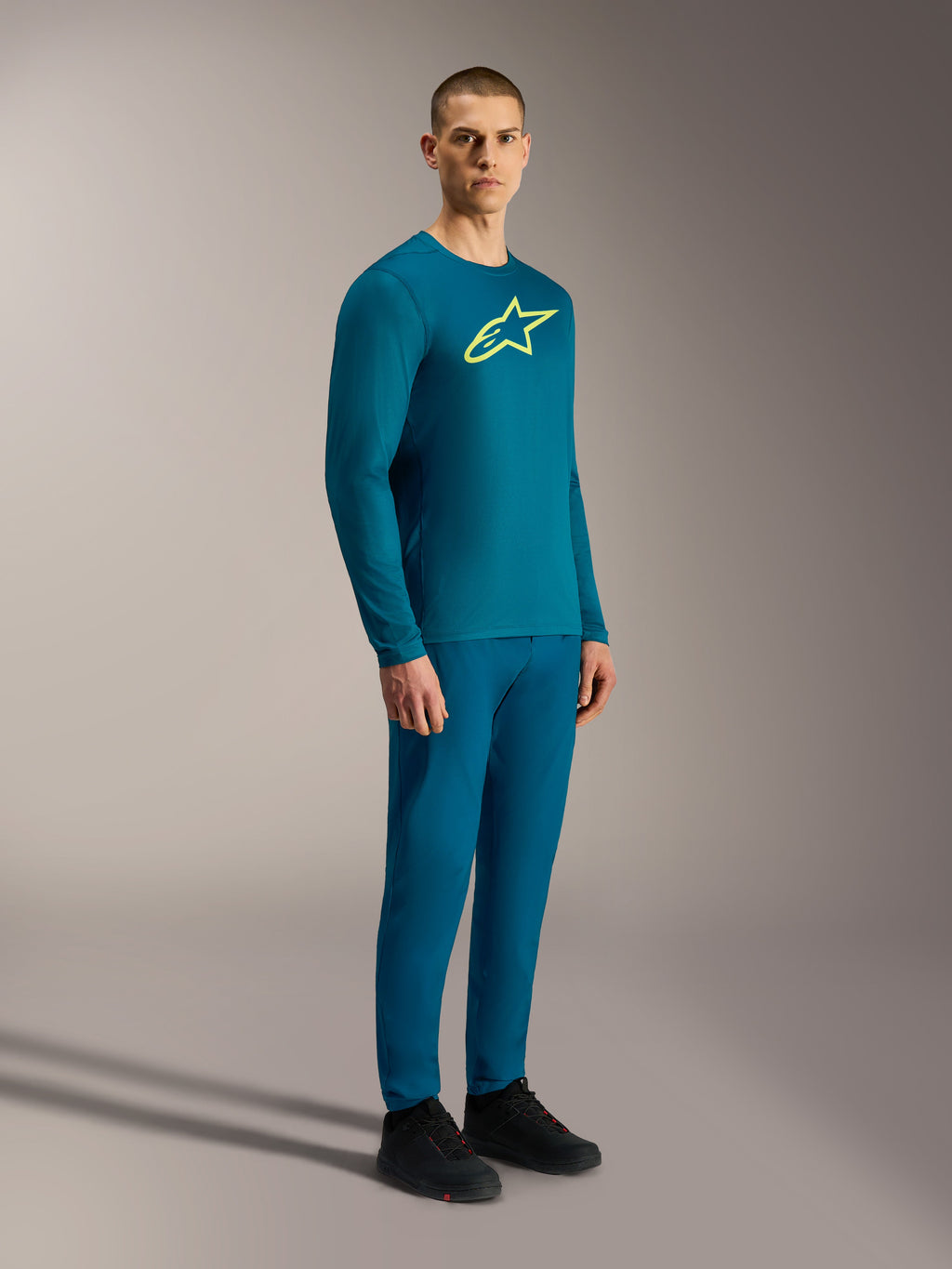 A-Dura Ride Langarmtrikot in Blau-Grün mit gelbem Astars-Logo, getragen mit passender Performance-MTB-Ausrüstung.