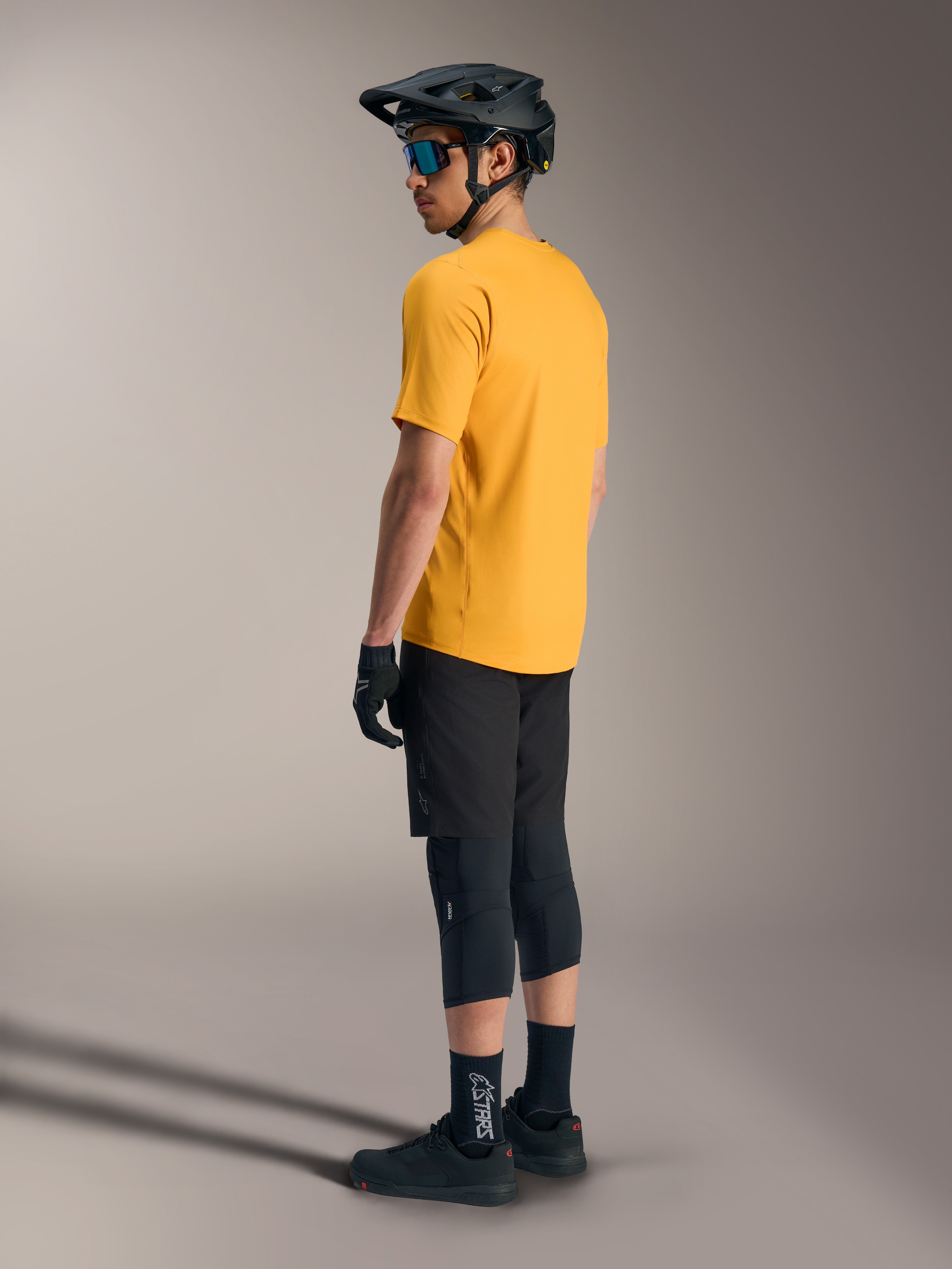Alpinestars A-Dura Ride Kurzarmtrikot in Orange, Rückansicht eines Fahrers mit schwarzer MTB-Ausrüstung und Helm.
