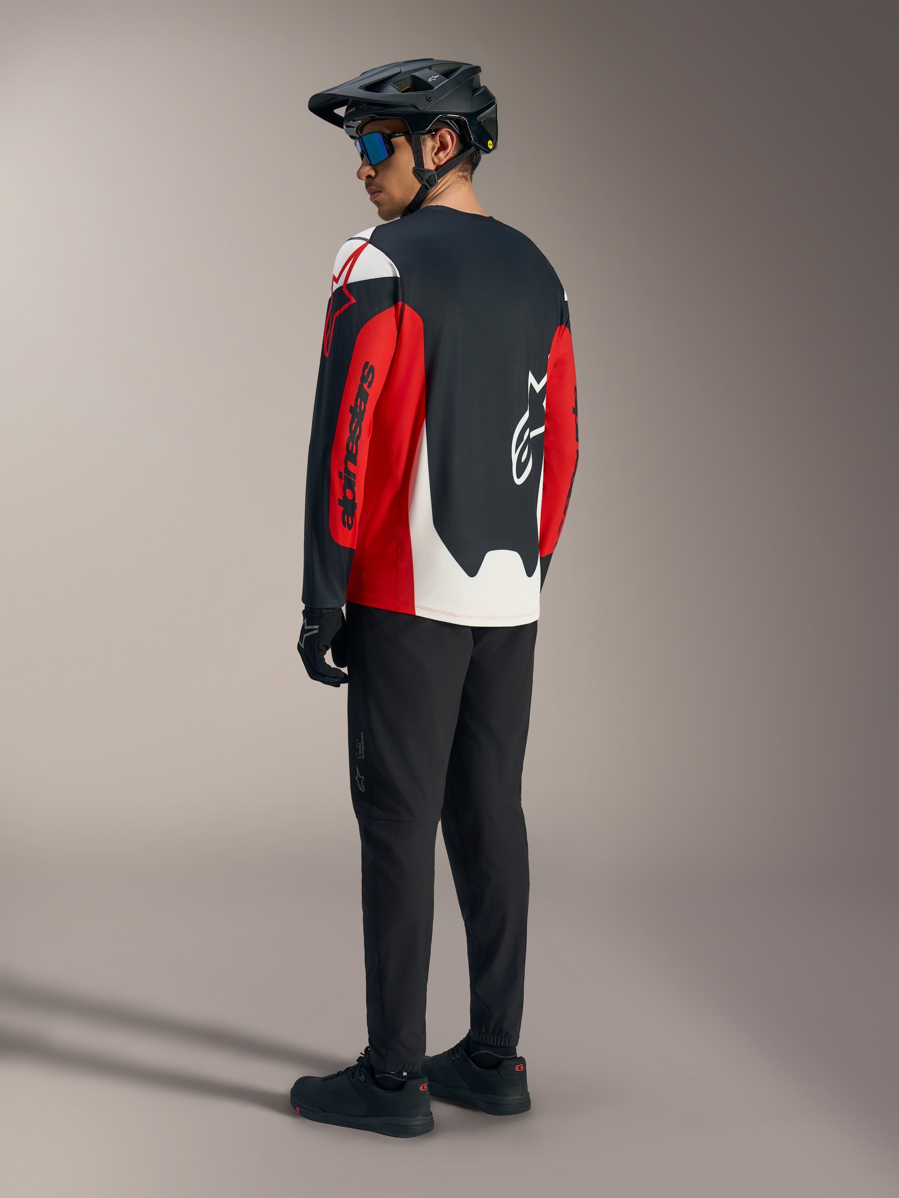 Rotes A-Dura Race Langarmtrikot mit Alpinestars-Grafiken, Rückansicht in einem Mountainbike-Outfit.