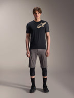 Alpinestars A-Dura Lipan Kurzarmtrikot, Schwarz mit grau melierten Ärmeln und beigem Astars-Logo auf der Brust, getragen von einem männlichen Model mit grauen Mountainbike-Shorts und schwarzen Knieprotektoren, Performance-MTB-Ausrüstung