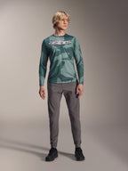 Alpinestars A-Dura Hollow Camo Langarm-Trikot, Silver Pine Camo mit grünem Camouflage-Muster, großes weißes „astars“-Logo auf der Brust, getragen mit grauer technischer Hose und schwarzen Radschuhen, Hochleistungs-MTB-Ausrüstung