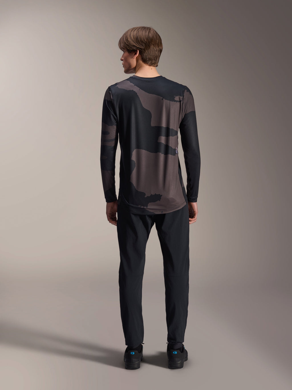 Alpinestars A-Dura Hollow Camo Langarm-Trikot, Black Camo, Rückansicht getragen mit schwarzer Hose, mit dunklem Camouflage-Muster und verlängertem Rückensaum für MTB-Abdeckung.