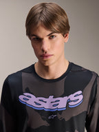 Alpinestars A-Dura Hollow Camo Jersey – Langarm, Schwarz-Camo mit lila 'astars' Grafik auf der Brust, Studioaufnahme eines männlichen Models in MTB-Bekleidung, lässiger und technischer Mountainbike-Stil