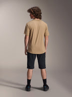 Male rider seen from the back wearing the Alpinestars A-Dura Astar Short Sleeve Jersey in Light Brown, paired with black mountain bike shorts and black socks, casual MTB trail riding style.