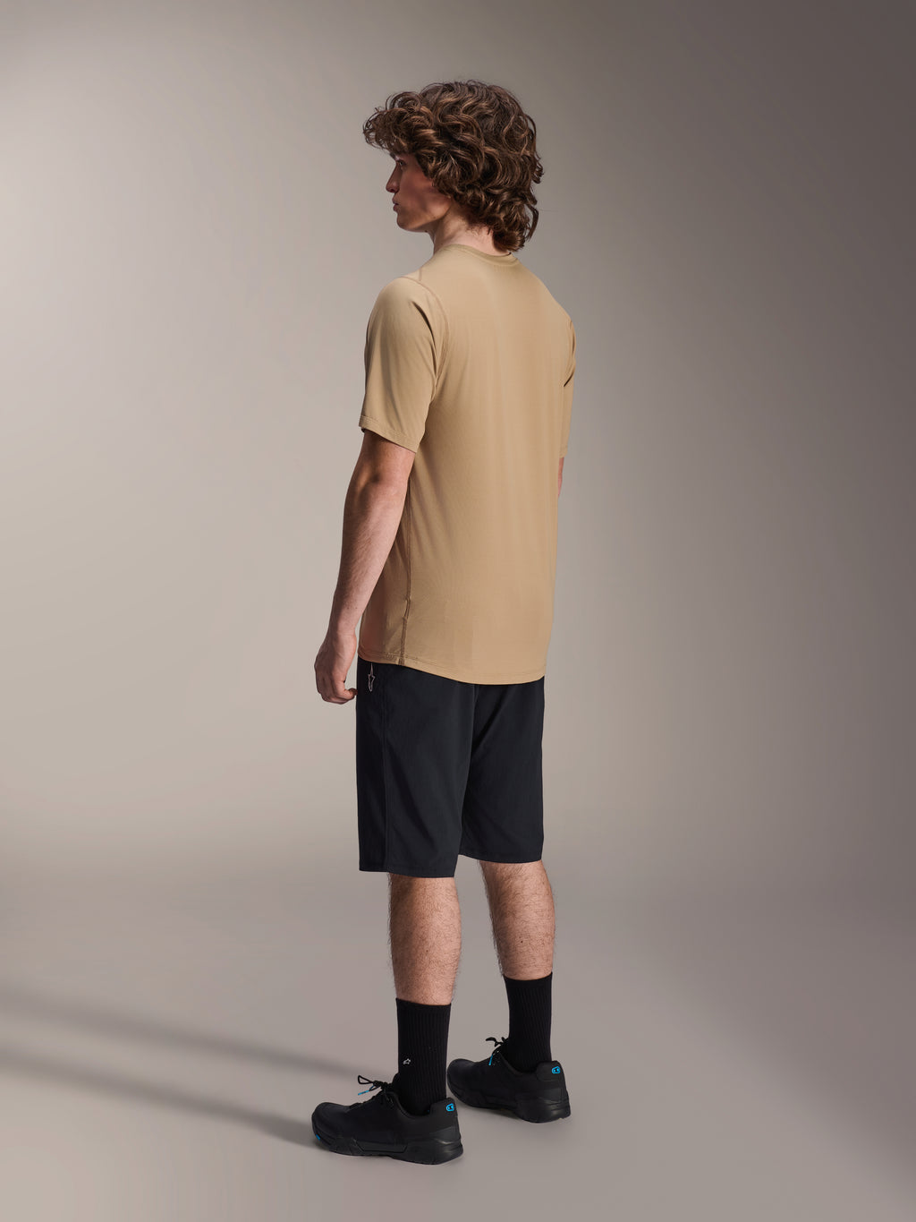 Alpinestars A-Dura Liner Shorts in Black and A-Dura SS Jersey in Tan, worn by a male model from a side profile view, paired with black socks and cycling shoes, mountain bike lifestyle apparel.