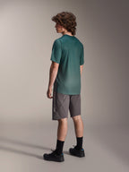 Alpinestars A-Dura Rise Trikot, Kurzarm-MTB-Trikot, Silver Pine Grün, getragen mit grauen Shorts und schwarzen Schuhen, Rückansicht mit verlängertem Rückensaum und regulärer Passform, leichtes, feuchtigkeitsableitendes Material für Trailfahrten