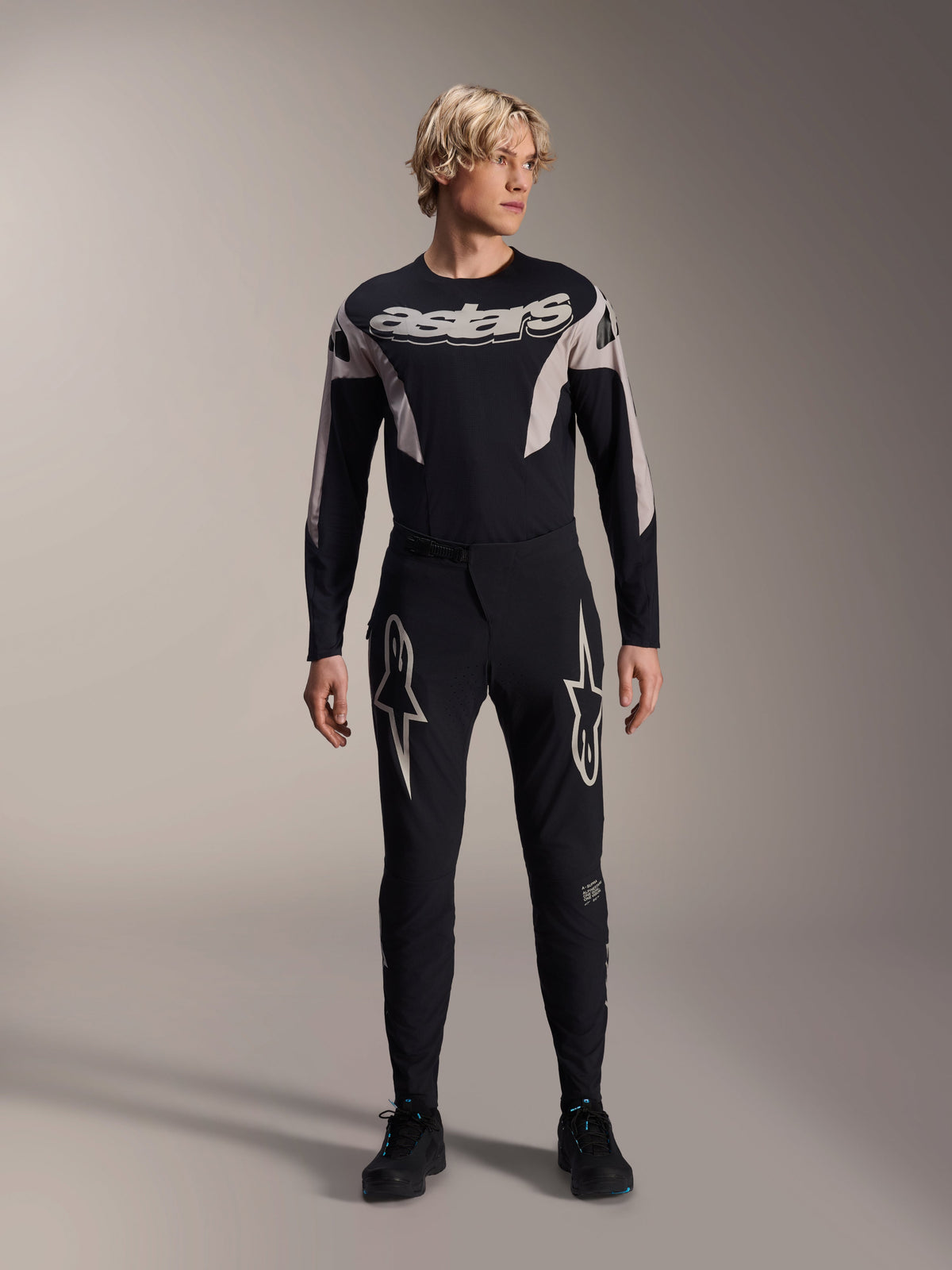Alpinestars A-Supra Melt Pants and matching Long Sleeve Jersey, model wearing black MTB kit with large white star graphics on thighs and 'astars' branding on chest, professional mountain bike racing apparel.
