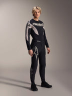 Male model wearing Alpinestars A-Supra Melt Pants and matching Long Sleeve Jersey, Black with light grey curved patterns, featuring bold white Astars logos on the legs and wordmark on the chest, professional mountain bike racing outfit.