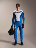 Männliches Model im Alpinestars A-Supra Melt MTB-Kit, weiß-blaues Langarmtrikot mit „astars“-Schriftzug, blaue A-Supra Melt Hose mit weißem Logo, schwarzer Full-Face-Helm, schwarze Handschuhe und Schuhe, abgestimmtes Offroad-Radsport-Outfit