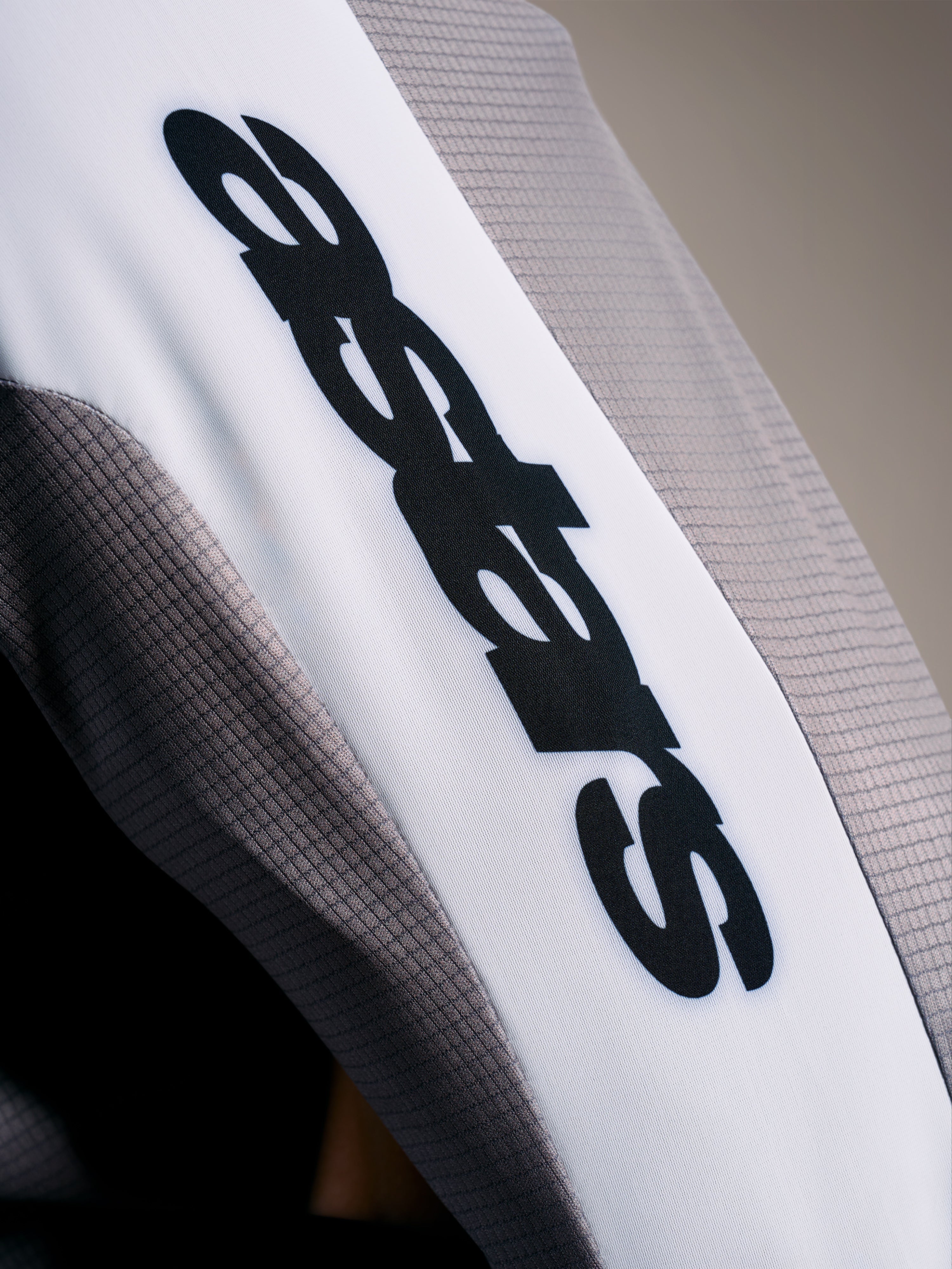 A-Supra Elite Trikot Detail, mikroperforiertes Gewebe in Faded Gray mit schwarzem ASTARS-Logo auf weißem Ärmelband.