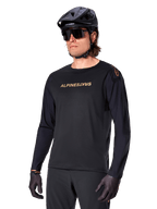 Alpinestars A-Aria Polartec Switch Long Sleeve Jersey, Black with gold logo, MTB mountain biking apparel, worn with a black helmet and sunglasses, featuring laser-cut ventilation on the sleeves and moisture-wicking Polartec fabric for off-road performance