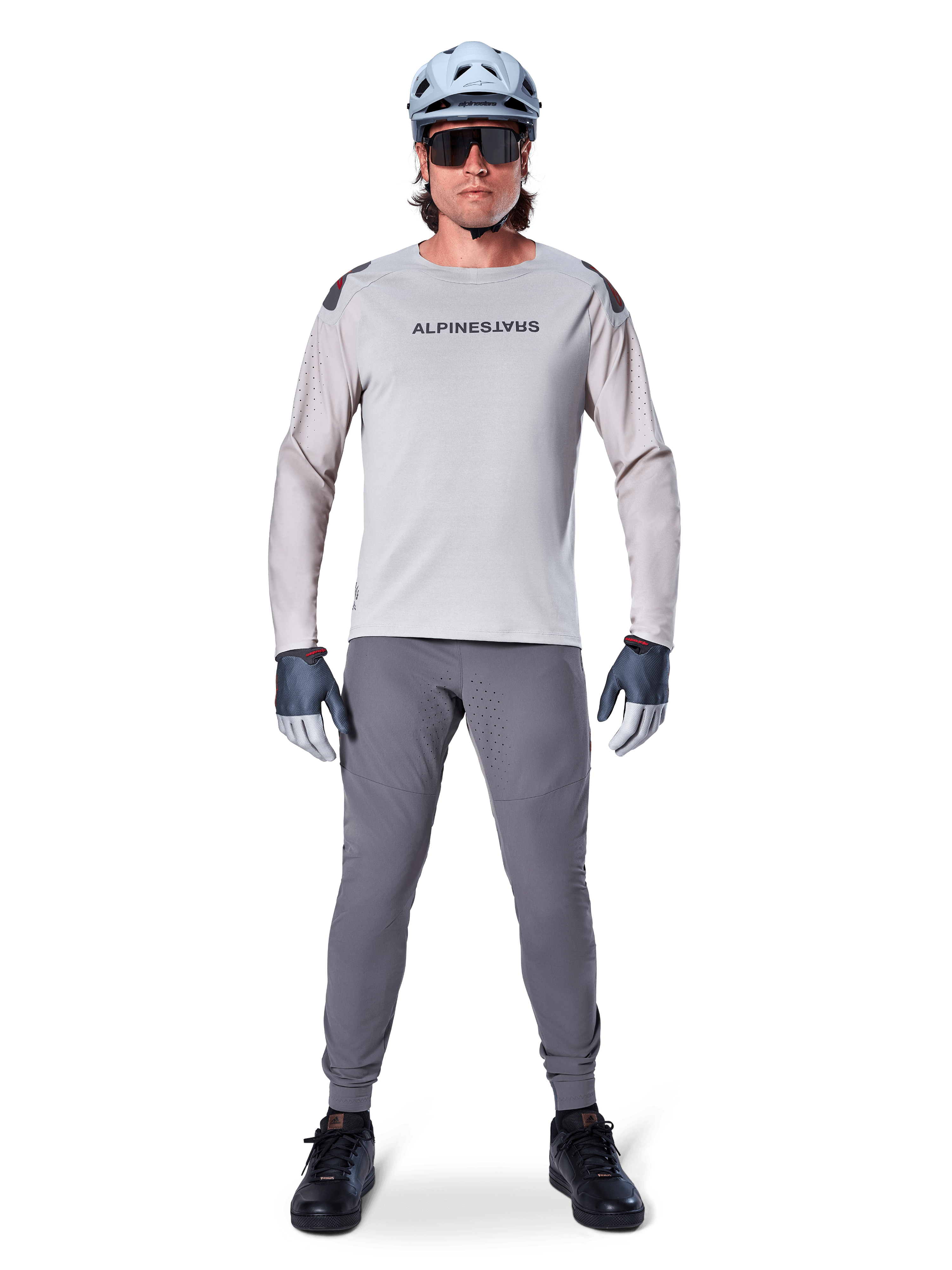 Alpinestars A-Aria Polartec Switch Jersey, Long Sleeve, Light Gray, worn by a male mountain bike rider with dark gray MTB pants, light blue helmet, and sunglasses, featuring chest branding and laser-perforated ventilation on the sleeves, complete off-road riding outfit.