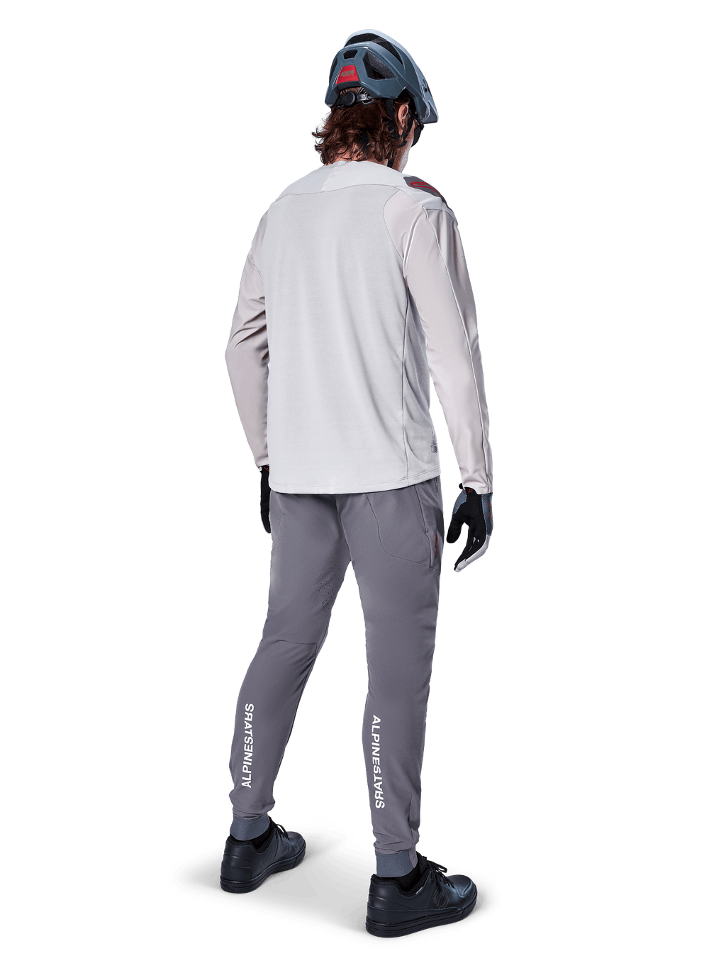 Rear view of a cyclist wearing the Alpinestars A-Aria Polartec Switch Long Sleeve Jersey in Light Gray, paired with dark gray mountain bike pants featuring white Alpinestars branding on the calves, black gloves, and a gray helmet.
