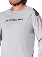 Close-up of the Alpinestars A-Aria Polartec Switch Long Sleeve Jersey in Light Gray, featuring Alpinestars chest branding, red shoulder logo, and laser-perforated sleeves for airflow, premium mountain bike gear.