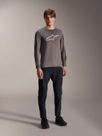 Alpinestars A-Dura Insert Astar Trikot, Langarm-MTB-Trikot, Dunkelgrau, mit großem weißem Brustlogo, getragen mit schwarzer technischer Hose und schwarzen Schuhen, Offroad-Radsportbekleidung
