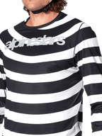Close-up of the Alpinestars A-Aria Oscar Long Sleeve Jersey in Black, featuring horizontal white stripes with a spiral Oscar graphic and a reflective silver Alpinestars logo across the chest, worn by a rider with a visible helmet strap.