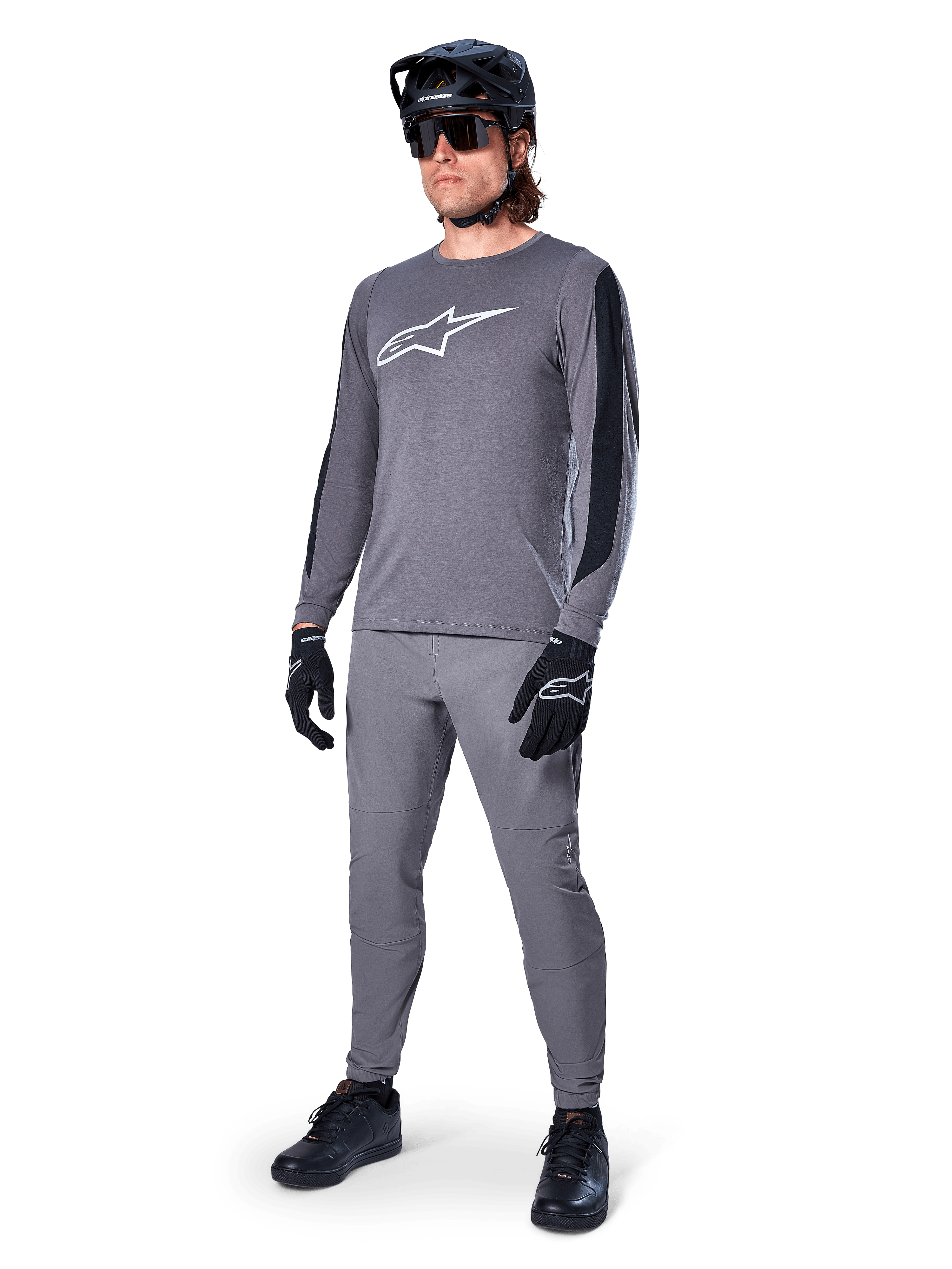 Alpinestars A-Dura Dri Astar Jersey, Long Sleeve MTB Jersey, Dark Gray with white chest logo, black mesh panels on sleeves, worn with matching gray pants, black helmet, and gloves, performance mountain bike apparel