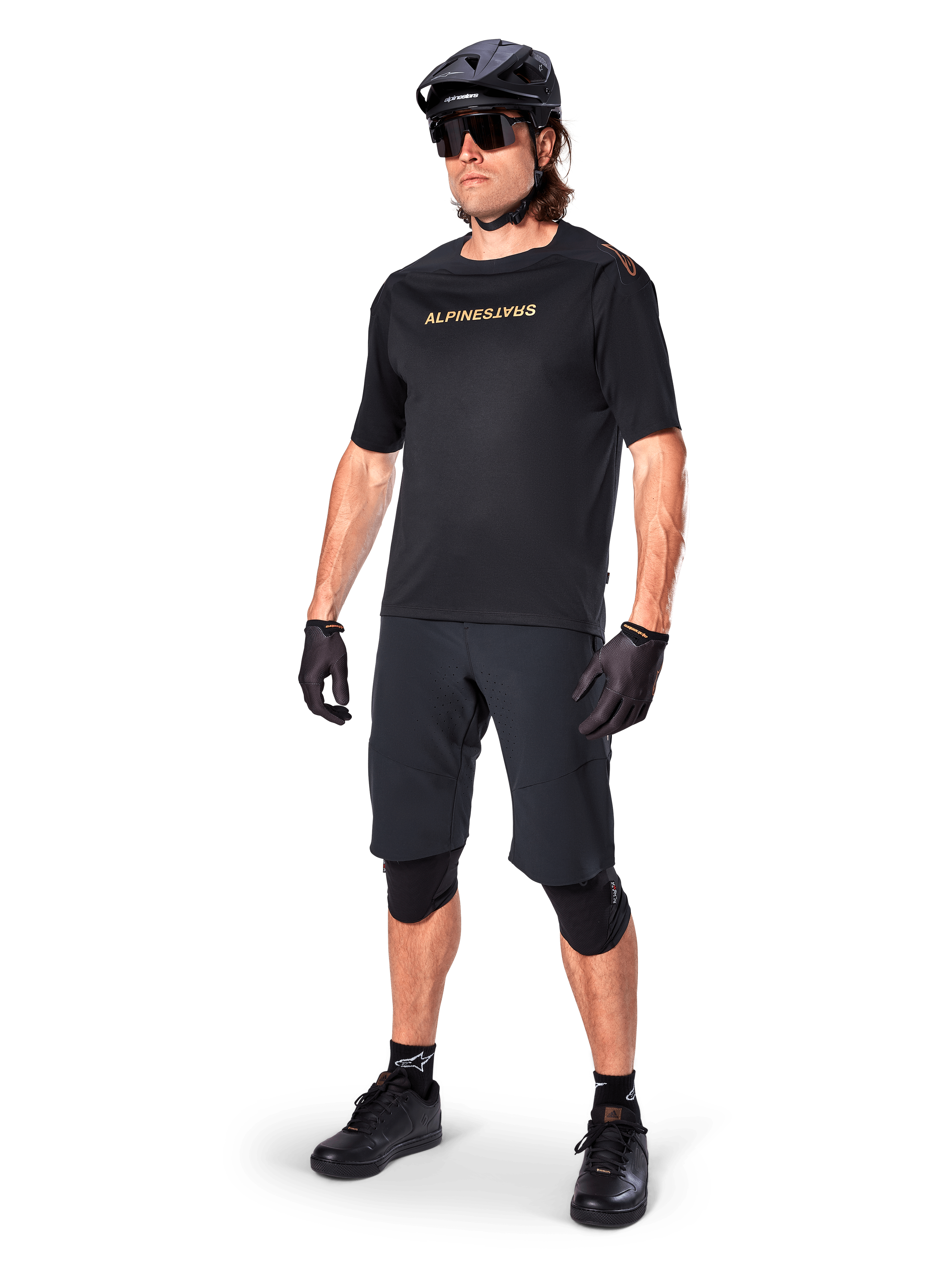 Alpinestars A-Aria Polartec Switch Short Sleeve Jersey, Black, featuring mirrored gold chest branding, worn by a rider with black cycling shorts, helmet, and knee pads, technical MTB gear for off-road performance