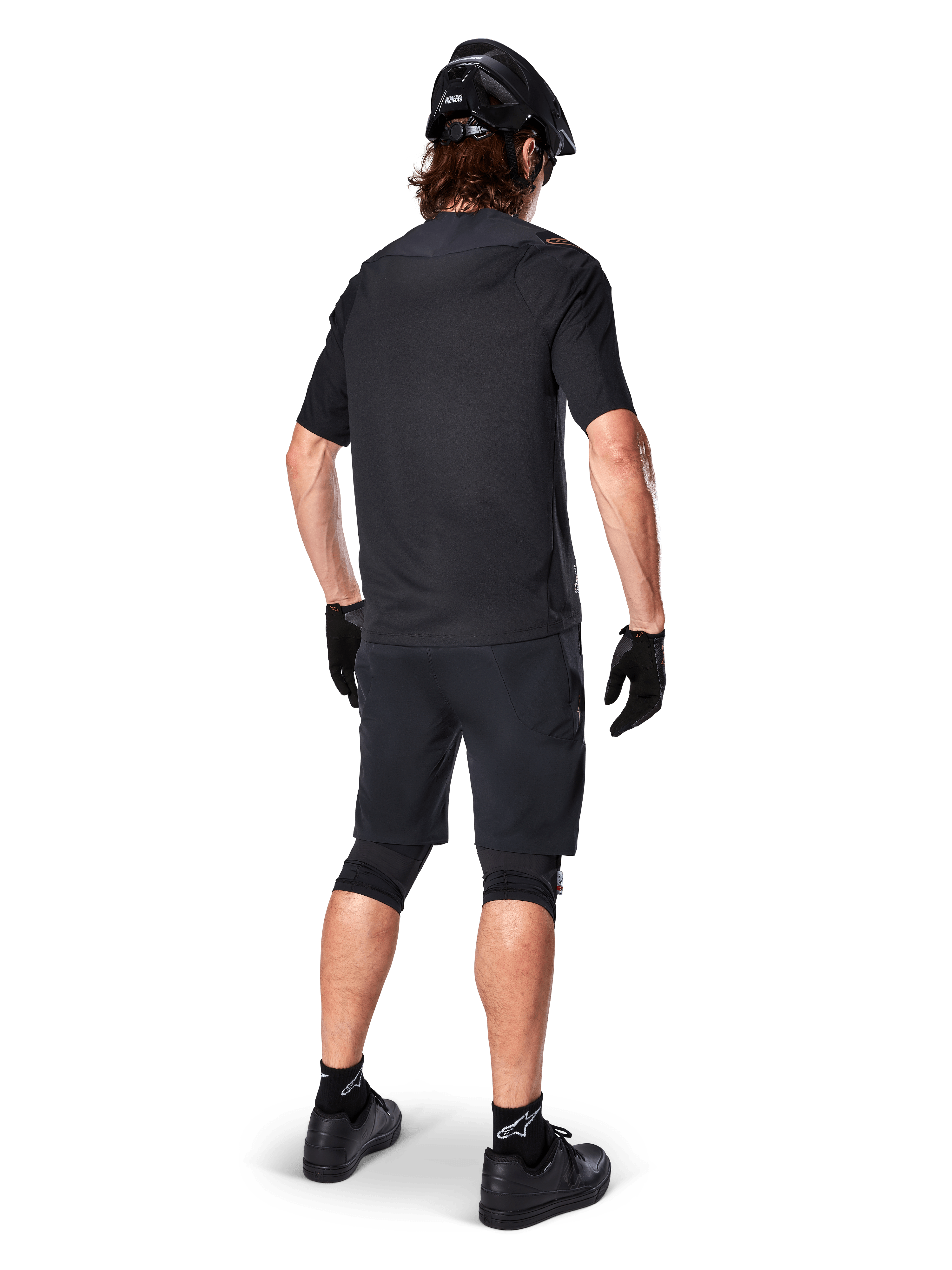 Male mountain bike rider from the back wearing the Alpinestars A-Aria Polartec Switch Jersey in black, short sleeve MTB jersey, paired with black mountain bike shorts, black helmet, and gloves, coordinated performance outfit for off-road trail riding