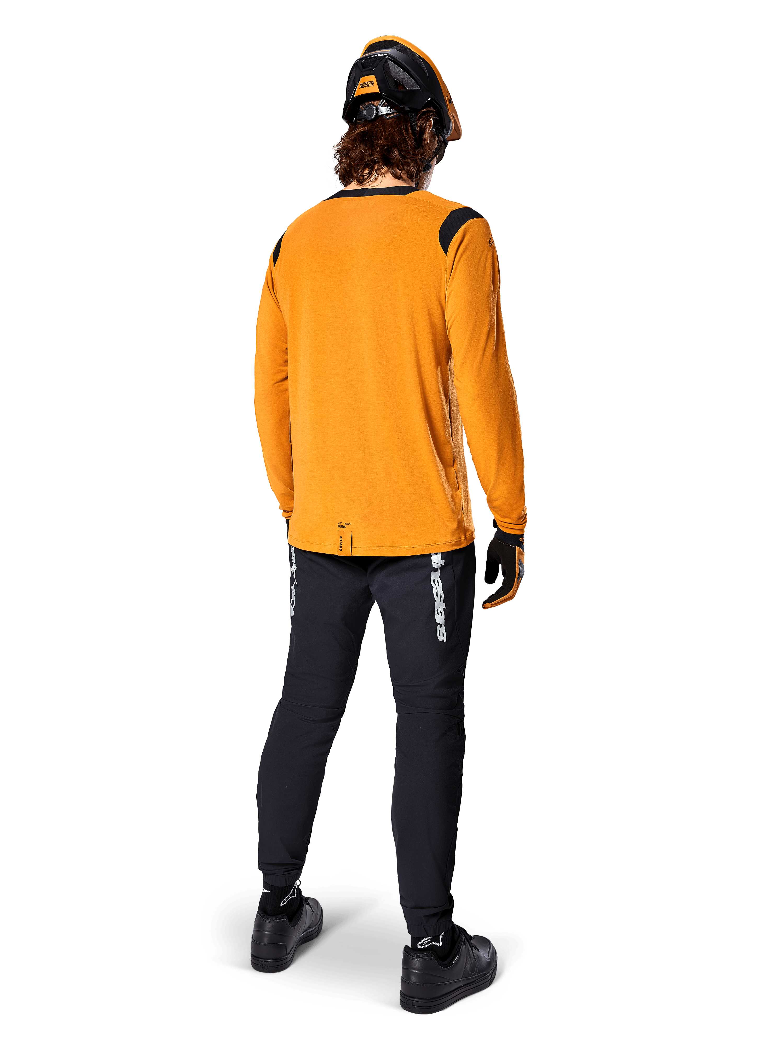 Mountain biker seen from behind wearing the Alpinestars A-Dura Dri Wool Long Sleeve Jersey in Dark Gold, black technical pants with white branding, and a coordinated black and orange helmet, performance-driven mountain bike apparel.