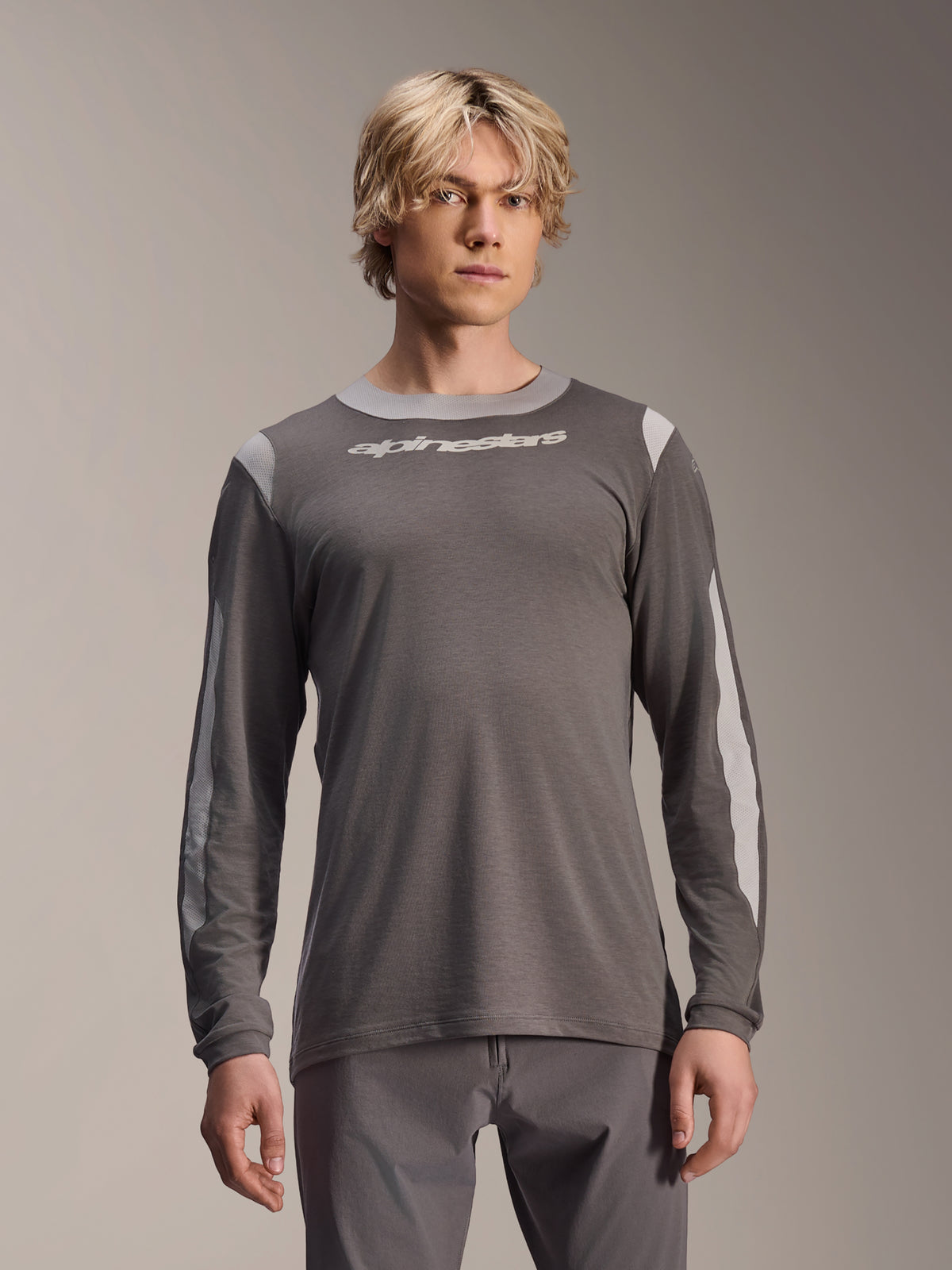 Alpinestars A-Dura Dri Wool Langarmtrikot, Dunkelgrau, getragen von einem männlichen Model, mit hellgrauen Mesh-Einsätzen an Schultern und Ärmeln, weißes Wortmarken-Logo auf der Brust, Performance-Mountainbike-Ausrüstung