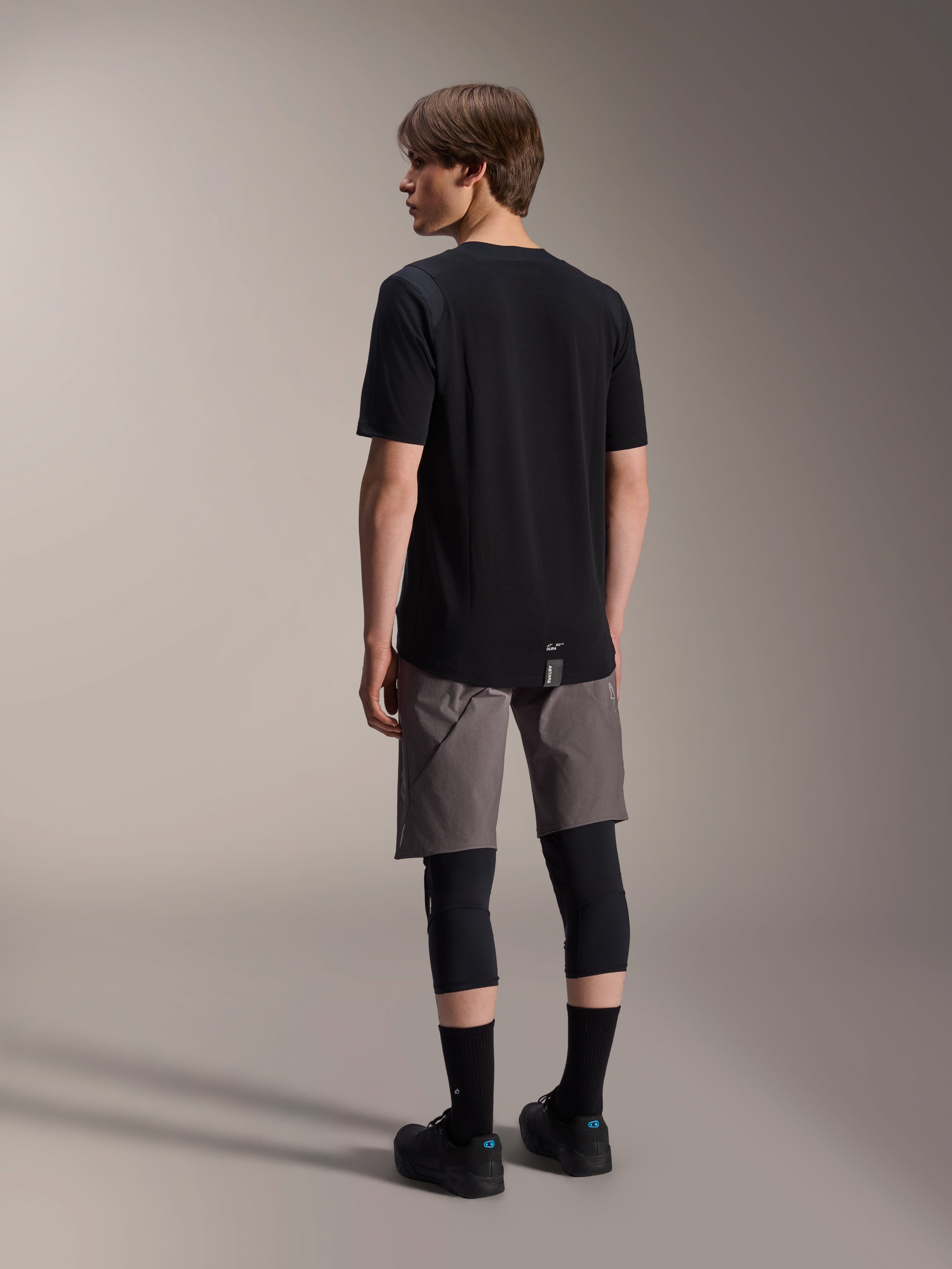 Alpinestars A-Dura Dri Wool Short Sleeve Jersey and A-Dura Elite Shorts, black and dark gray mountain bike apparel, worn with black knee guards and socks, back view of cycling gear for off-road performance